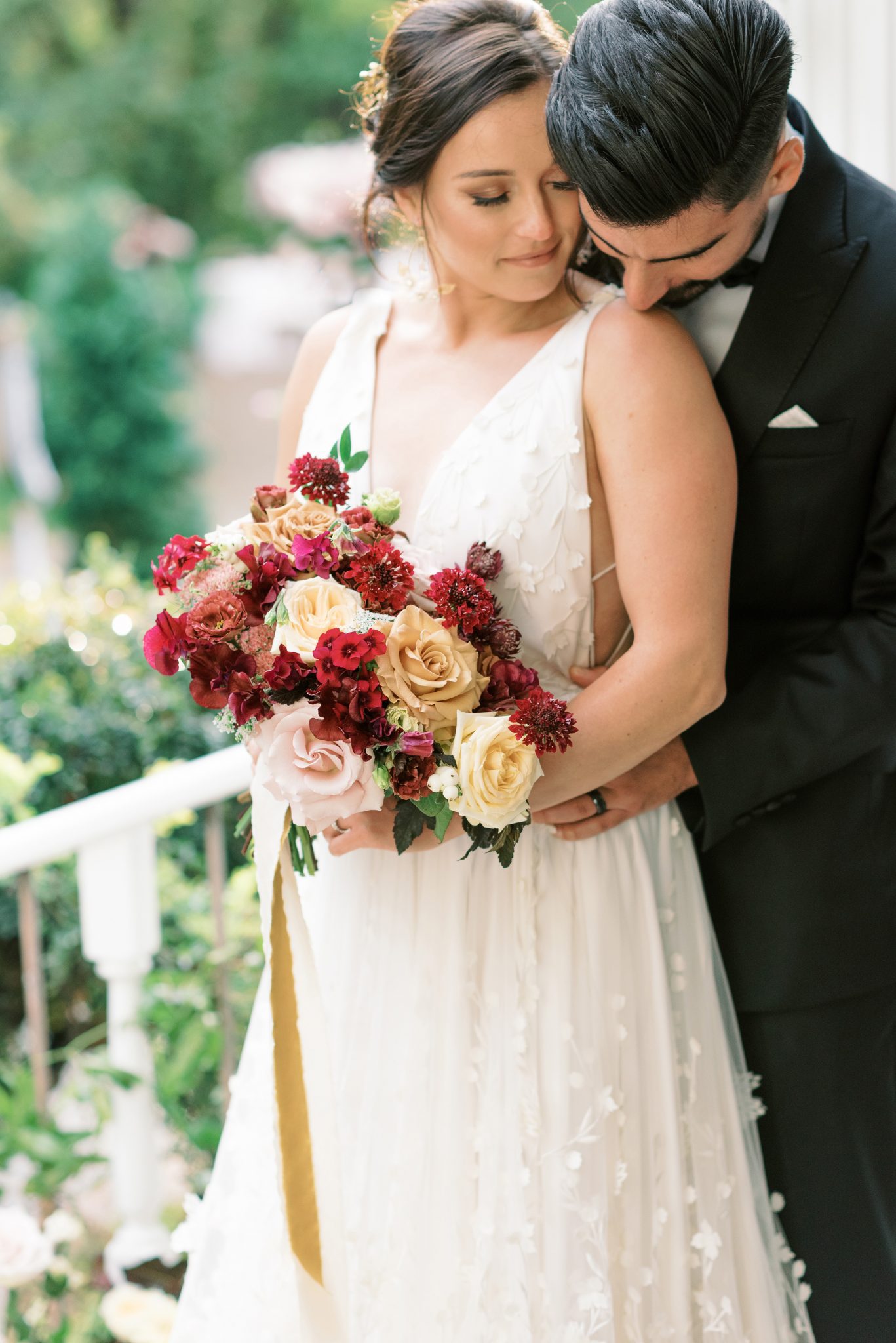 Bride and groom pose on the steps of the Norland Historic Estate with a bridal bouquet featuring berry and gold hues