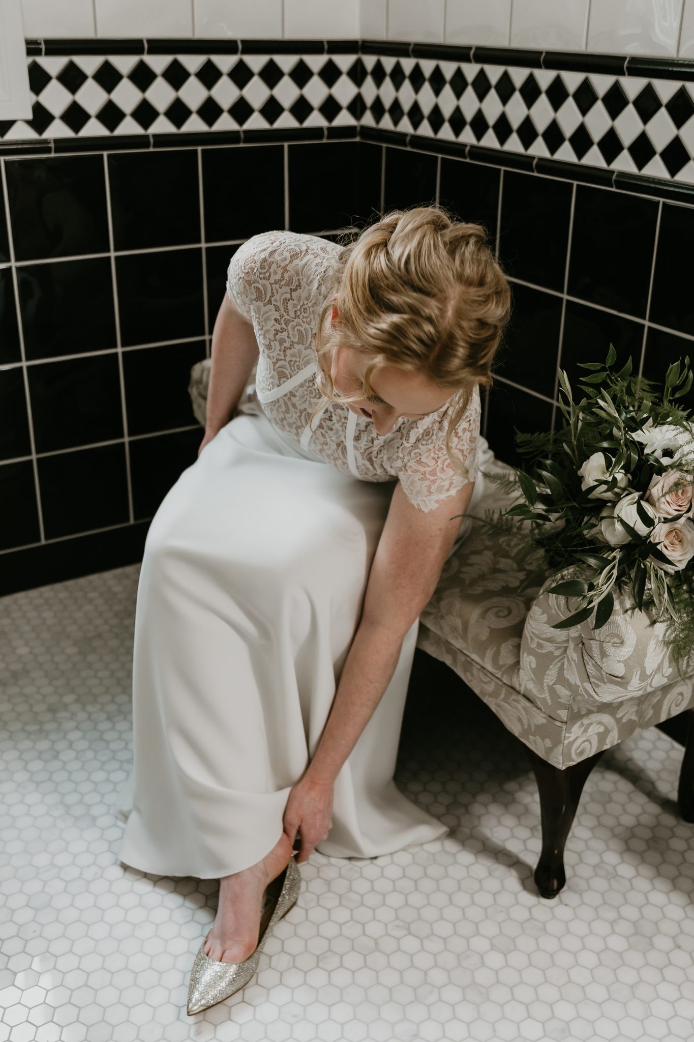 A bride in a crepe and lace gown puts her shoes on moments before her living room minimony