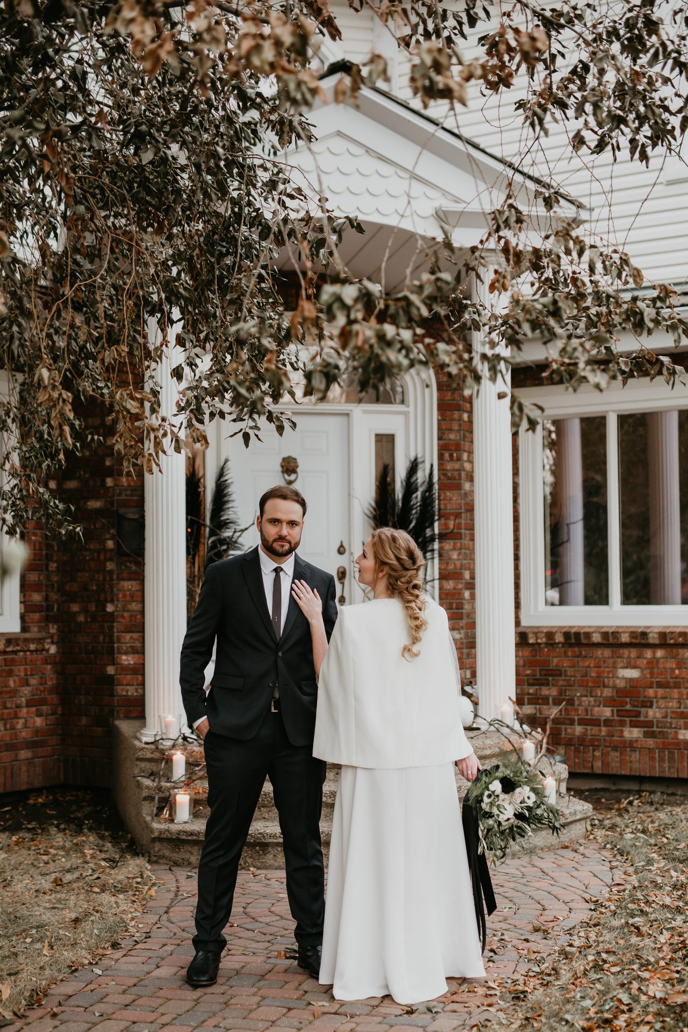Bride and groom pose in front of a St. Albert home after their living room minimony featuring a bridal cape