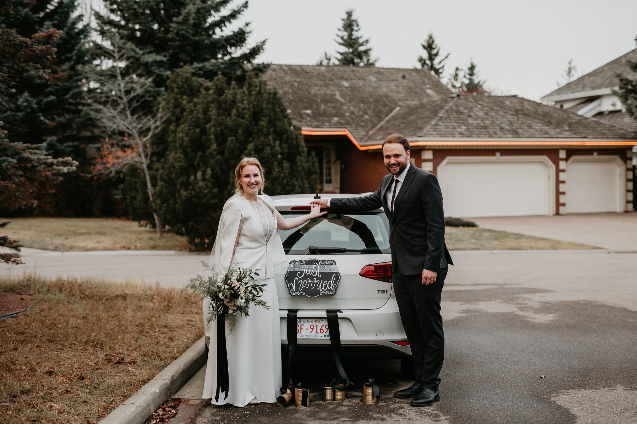 St. Albert bride and groom pose with a Just Married sign hanging on the back of their getaway car