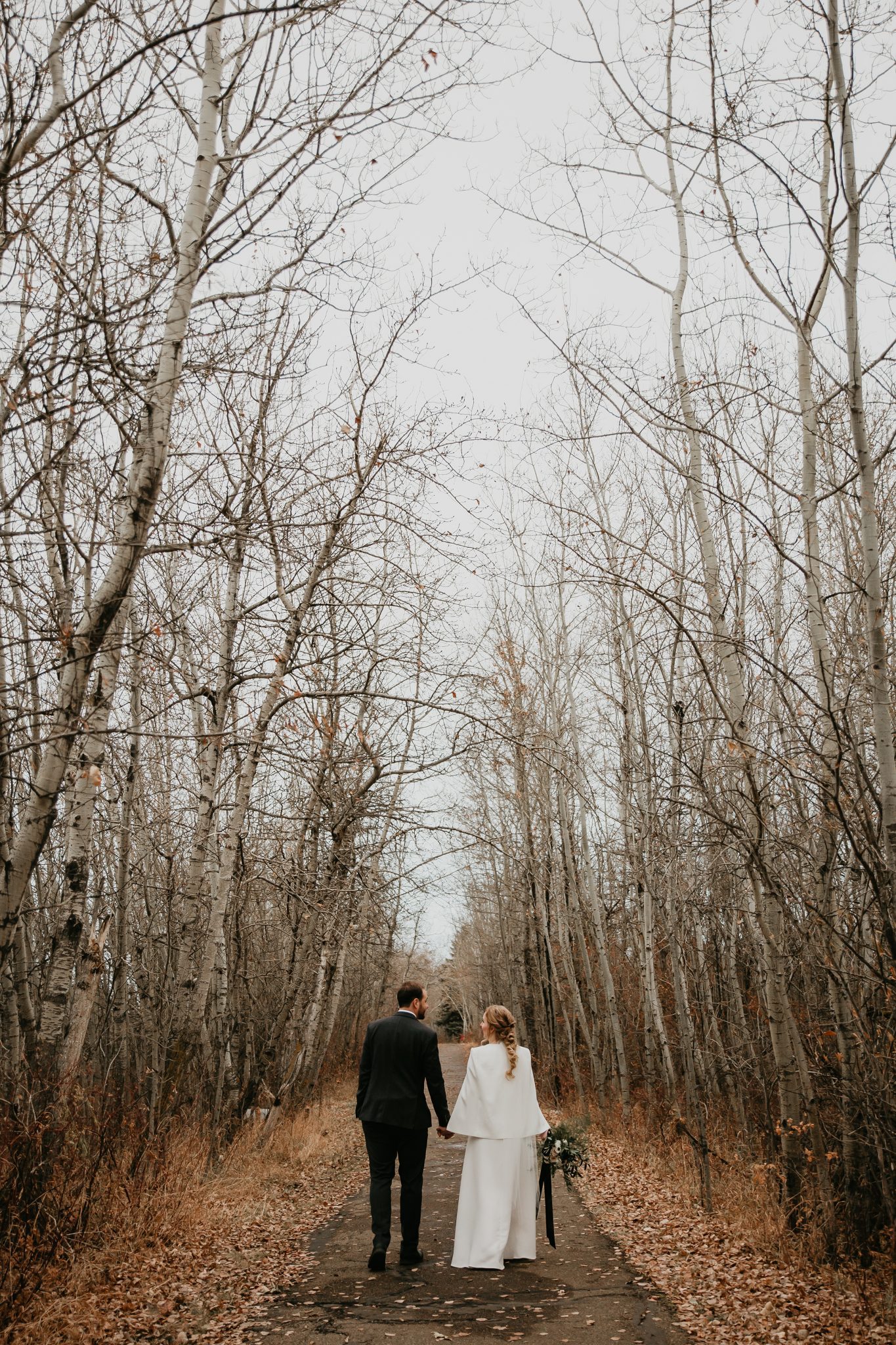Bride and groom walk down a tree lined path for their October fall wedding