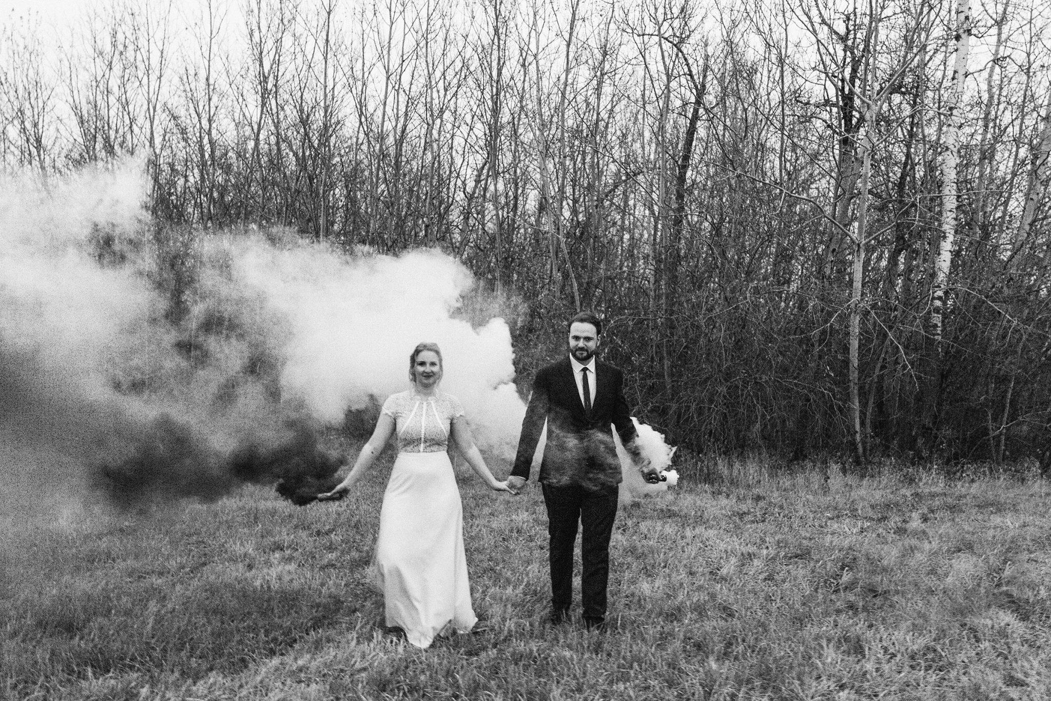 Black and white portrait of a bride and groom with smoke bombs in an autumn field
