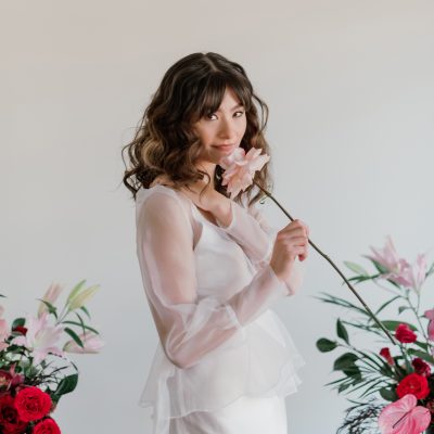 Bride with romantic wavy hair poses with a garden rose for this modern microwedding inspiration