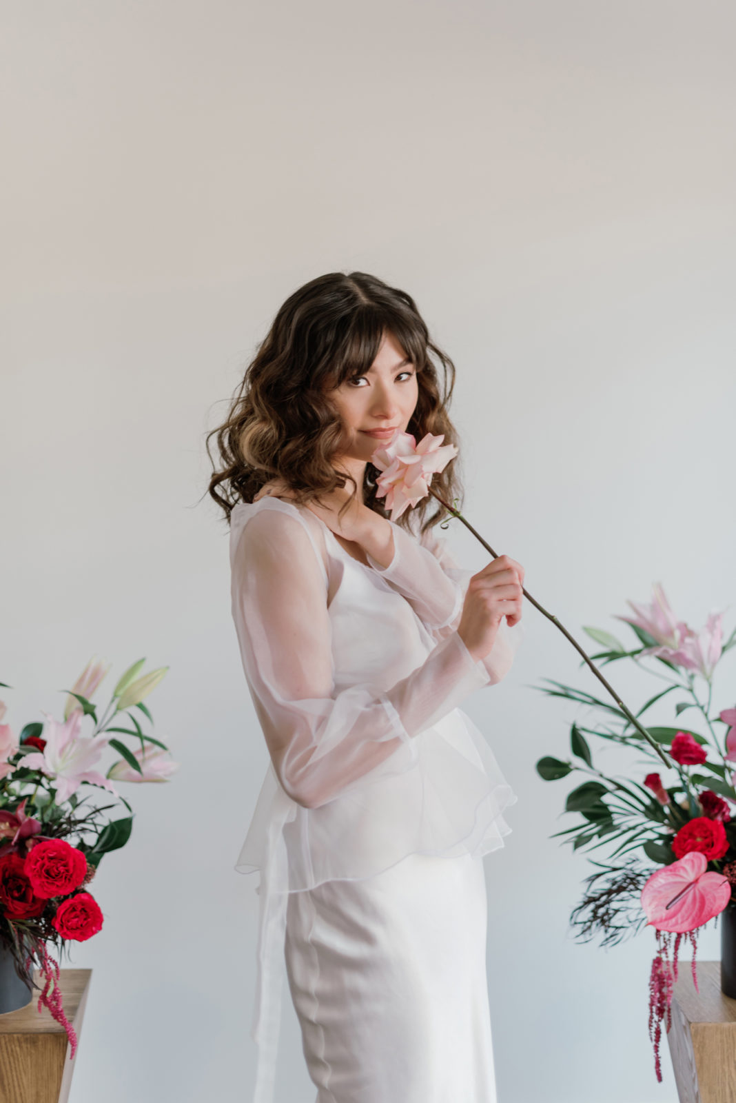 Bride with romantic wavy hair poses with a garden rose for this modern microwedding inspiration