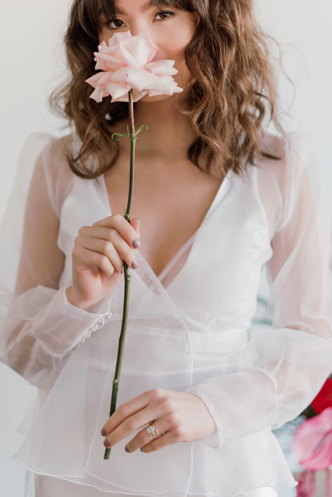 Bride in a shear sleeved gown poses with a pink rose