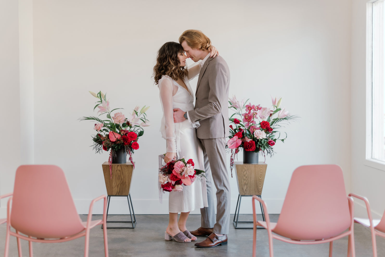 Bride in a short dress and a groom in a grey suit pose in front of modern microwedding ceremony inspiration