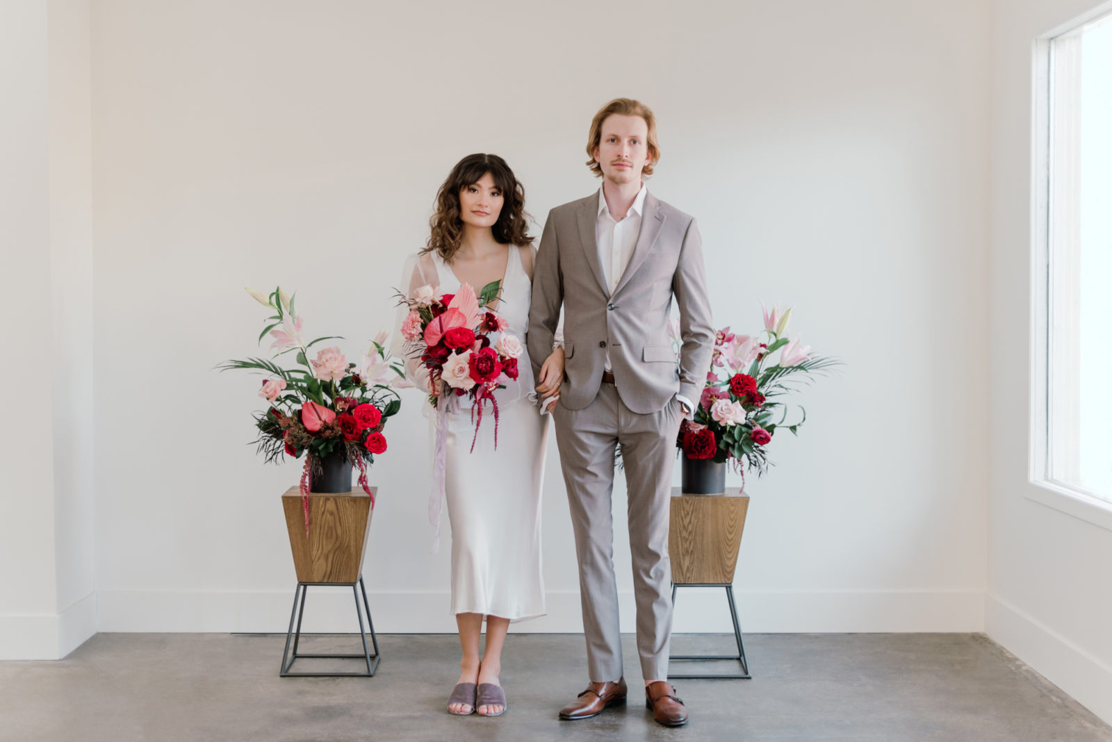Modern bride and groom pose in front of a ceremony display of vibrant flowers
