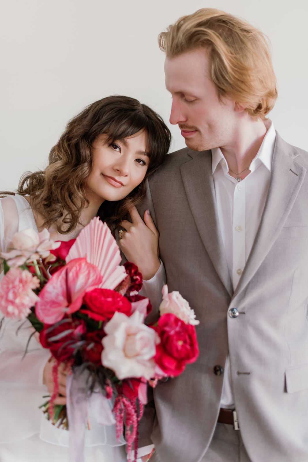 Bride and groom pose with a vibrant pink, red and white bridal bouquet