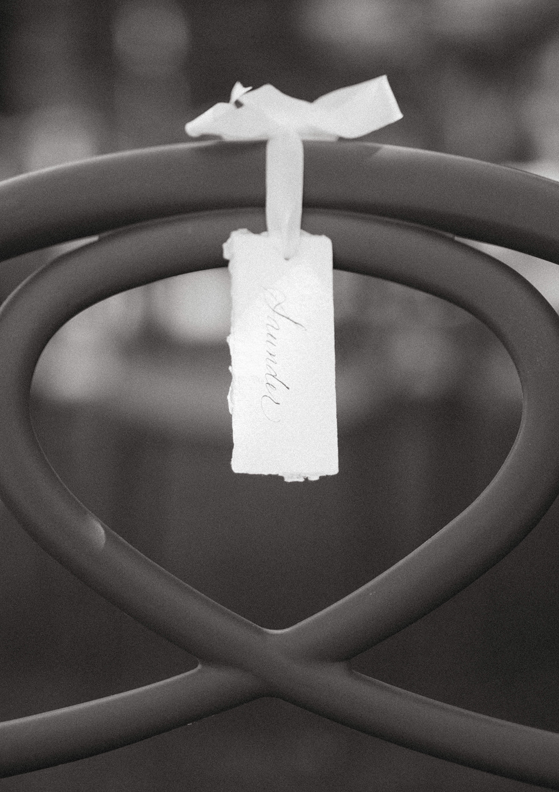Black and white photograph of a white ribbon name tag tied to a wedding ceremony chair