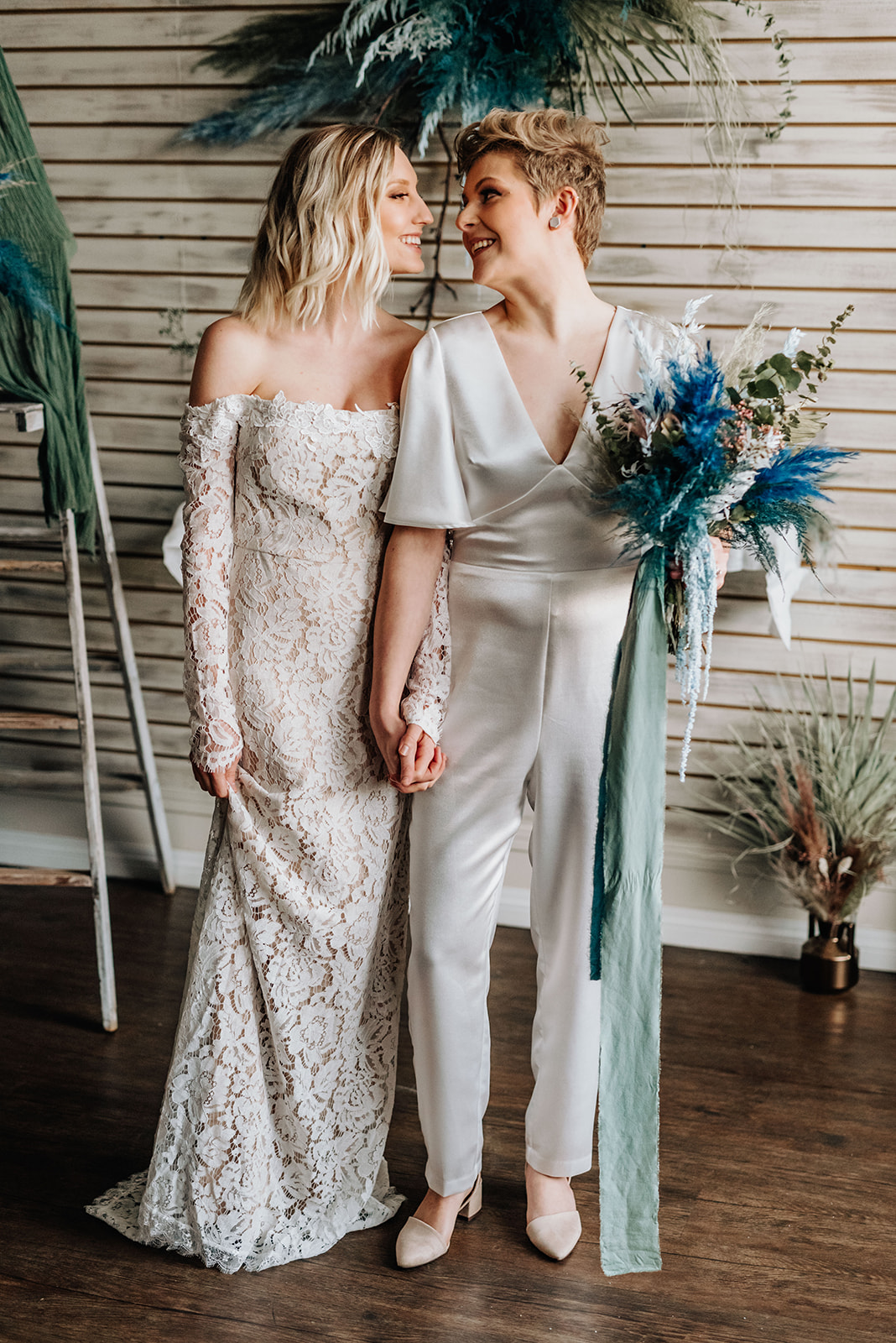 Brides pose hand in hand with a blue bohemian bouquet for this hair salon elopement