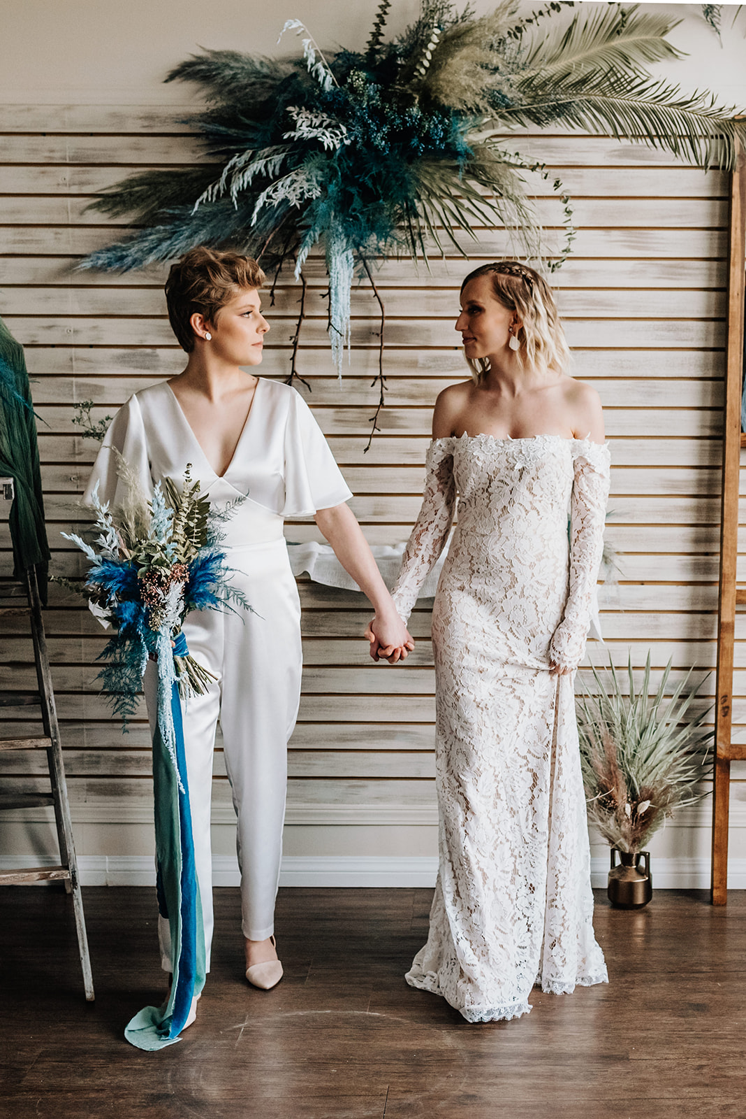 Chic brides pose hand in hand in front of their bohemian wedding decor