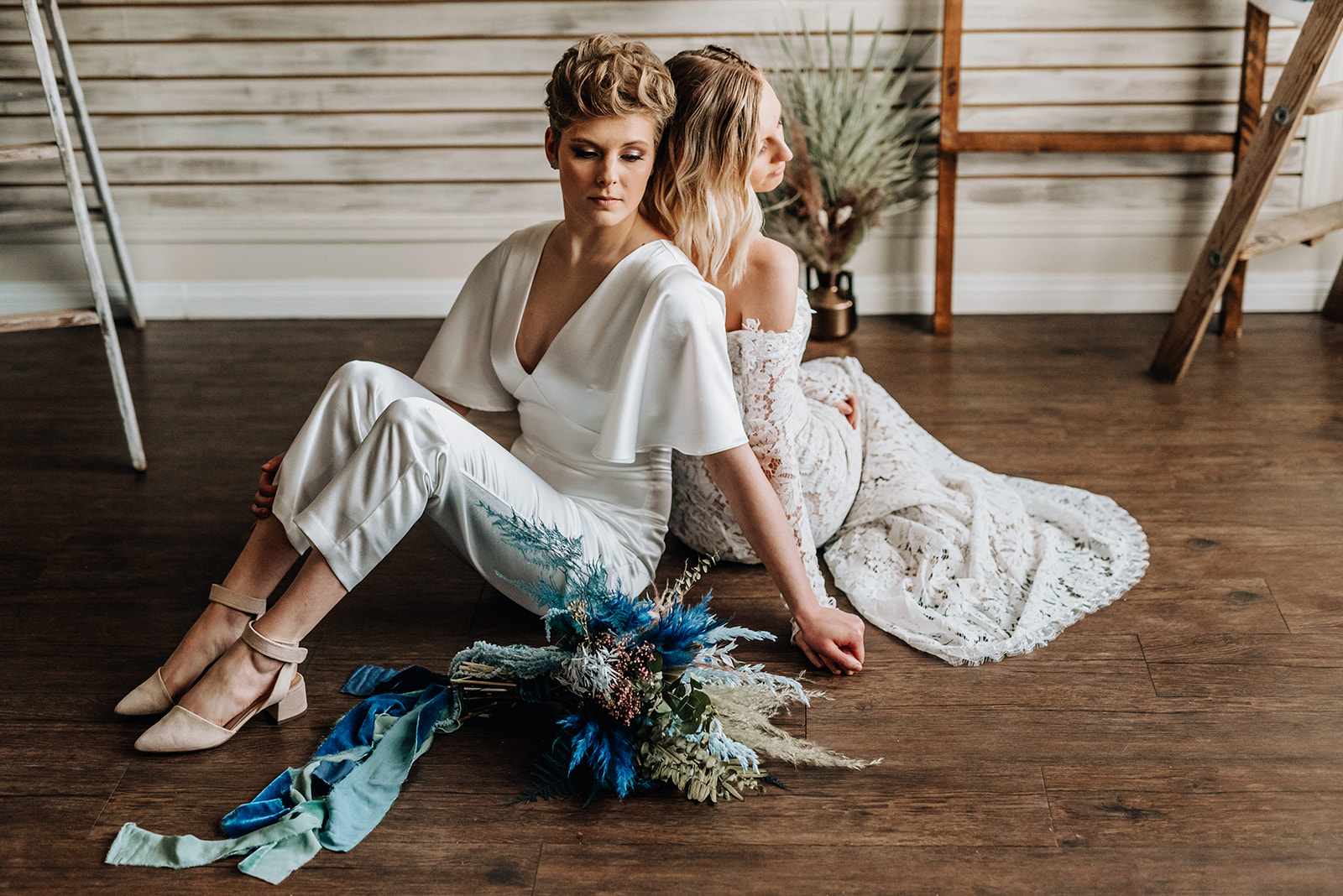 Chic bohemian brides pose seated with their backs to each other
