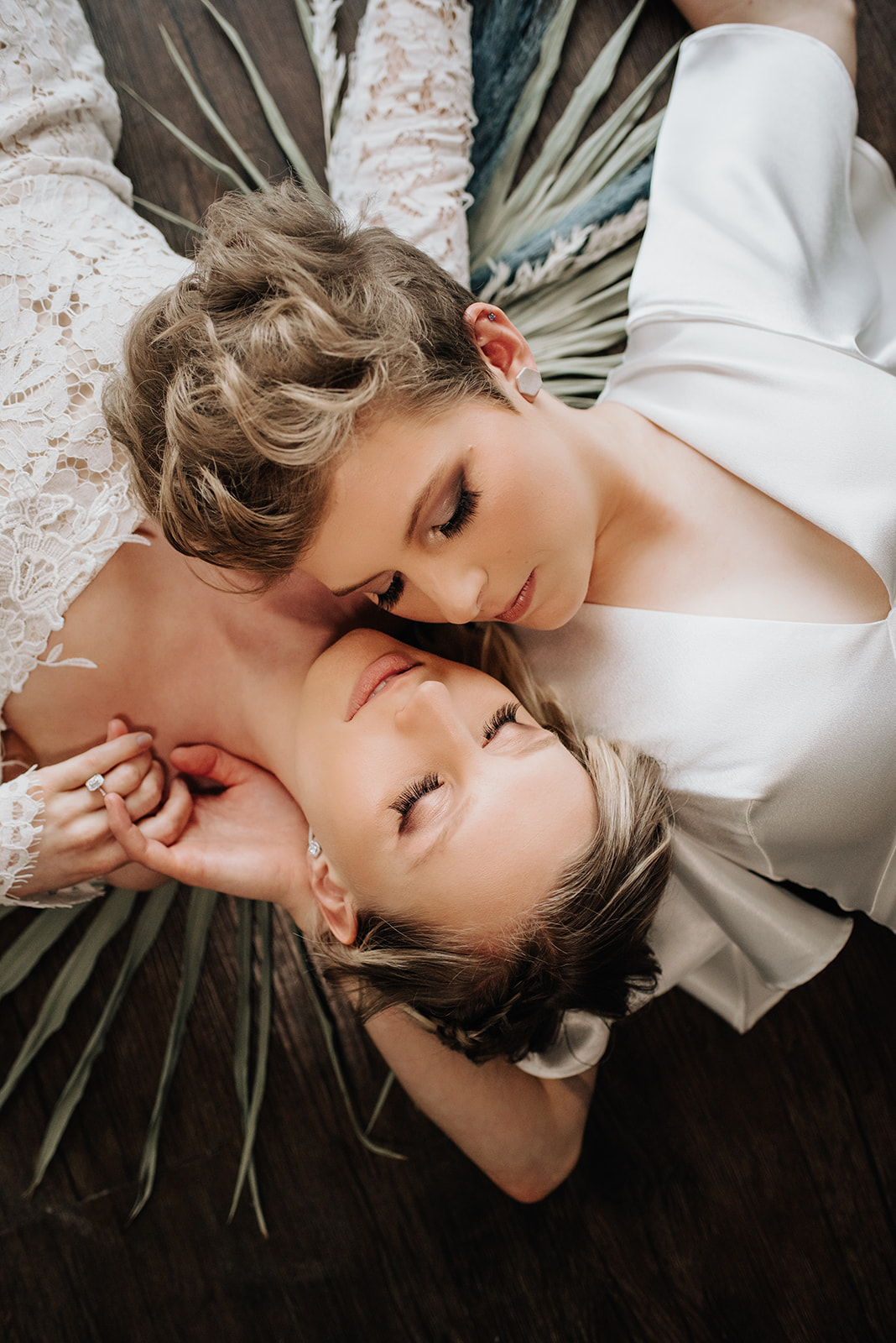Chic bohemian brides pose next to each other lying down with their backs to the floor