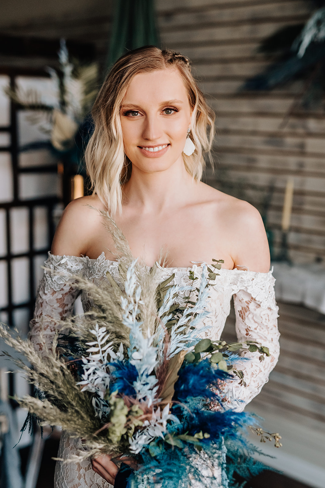 Bohemian bride in a lace off the shoulder wedding gown holds a bouquet featuring deep blue and dark teal florals