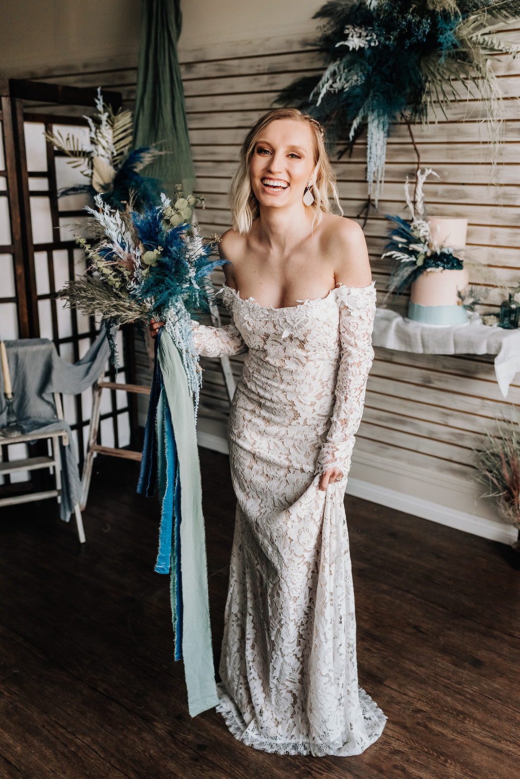 Bride in a lace gown and clay earrings poses with a bohemian bridal bouquet with deep blue and dark teal floral accents