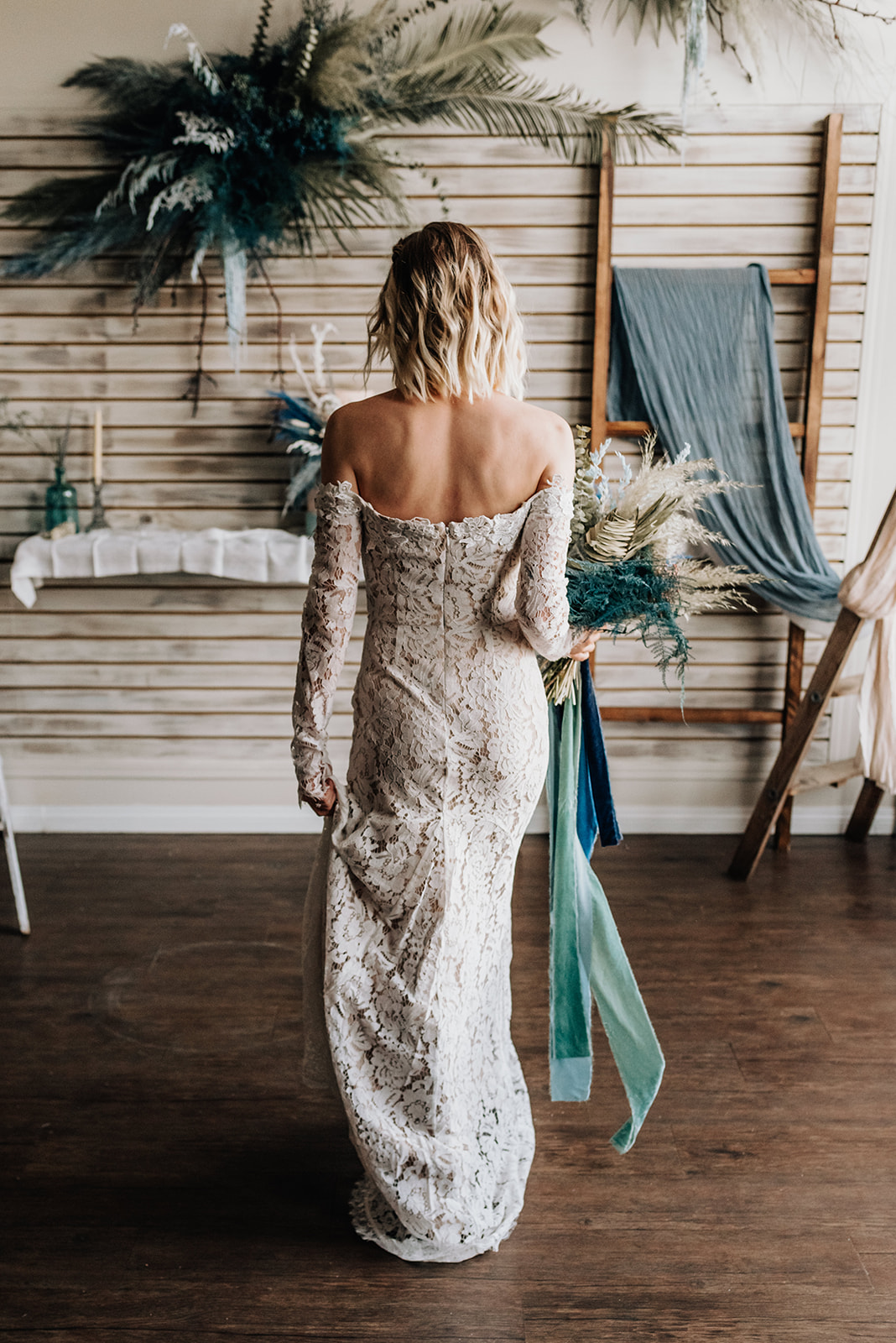 Bride in a lace gown poses in front of bohemian wedding decor with deep blue and dark teal accents 