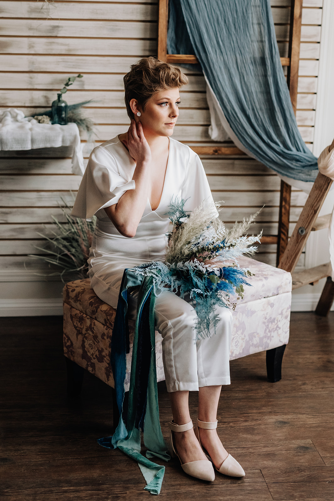 Bride poses seated with a blue and green boho bridal bouquet