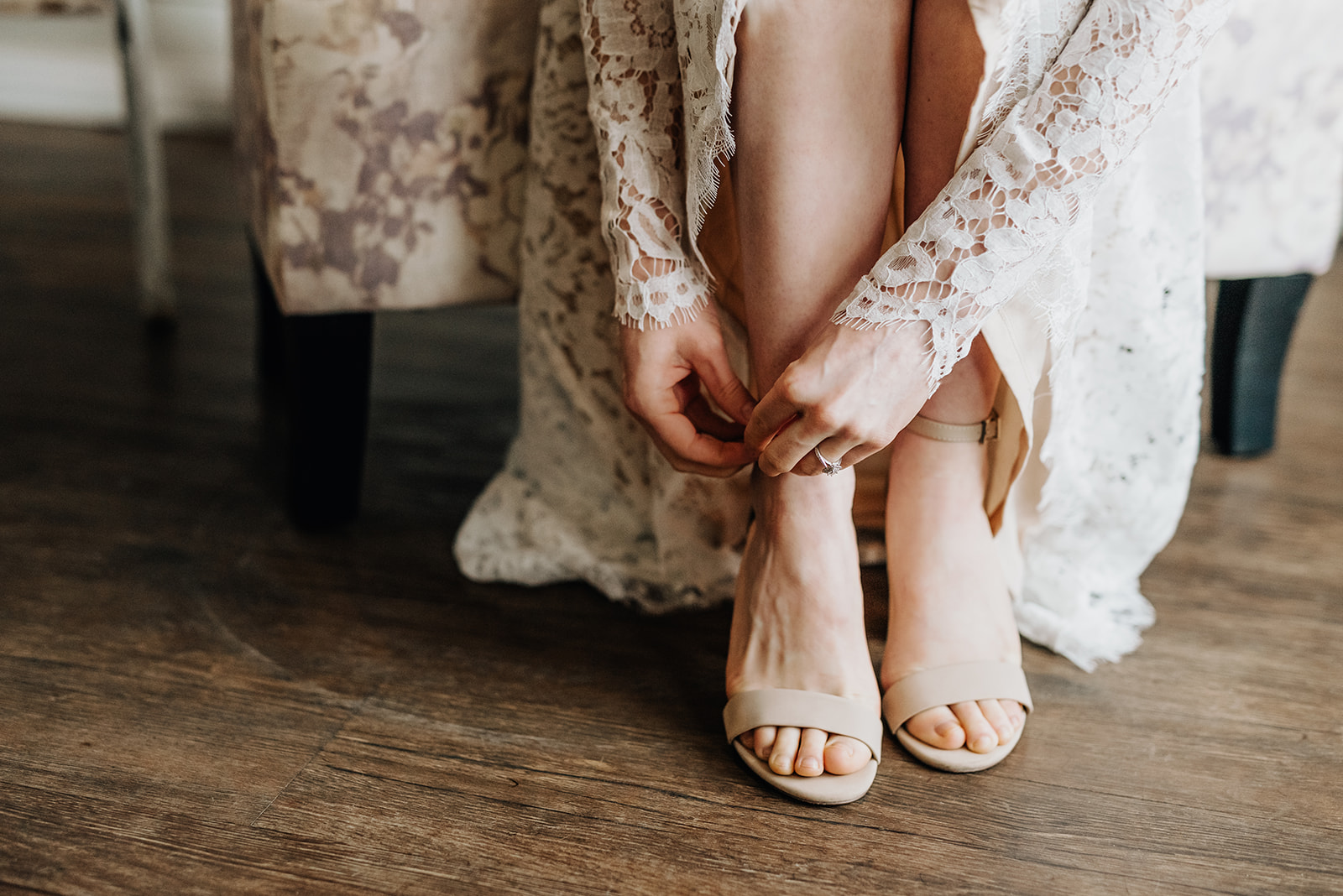 Bride in a lace wedding gown fastens the clasp on her nude high heels