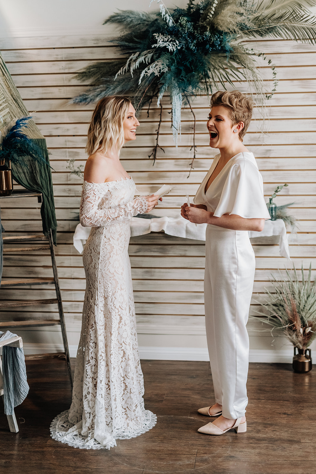 Brides laugh as they share their vows in front of their bohemian blue ceremony decor