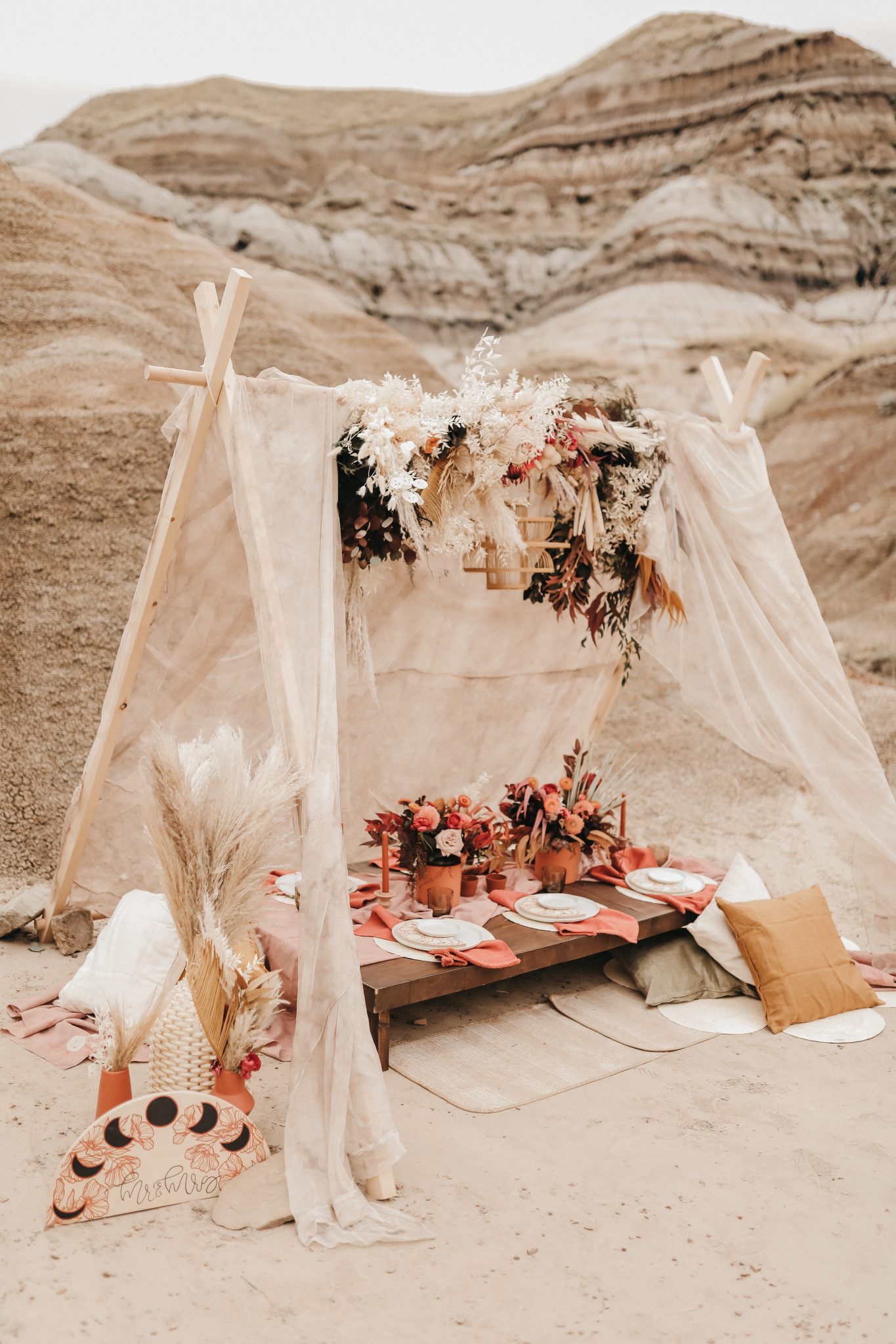 Moroccan inspired elopement tent with linen, pillows, boho terracotta flowers and a wicker chandeleir