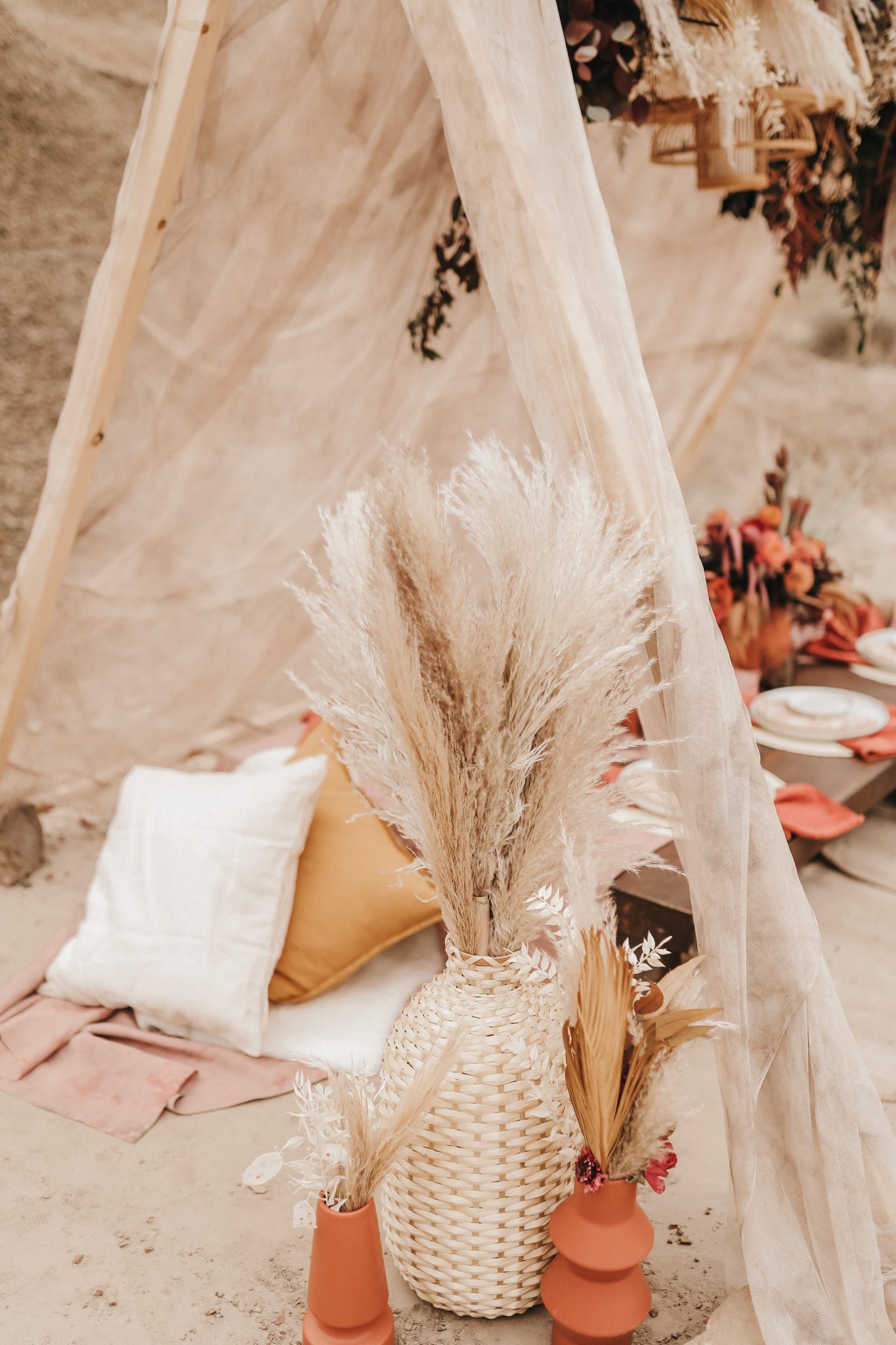 Pampas grass in a wicker vase in front of a linen tent with pillows and a Moroccan inspired elopement tablescape