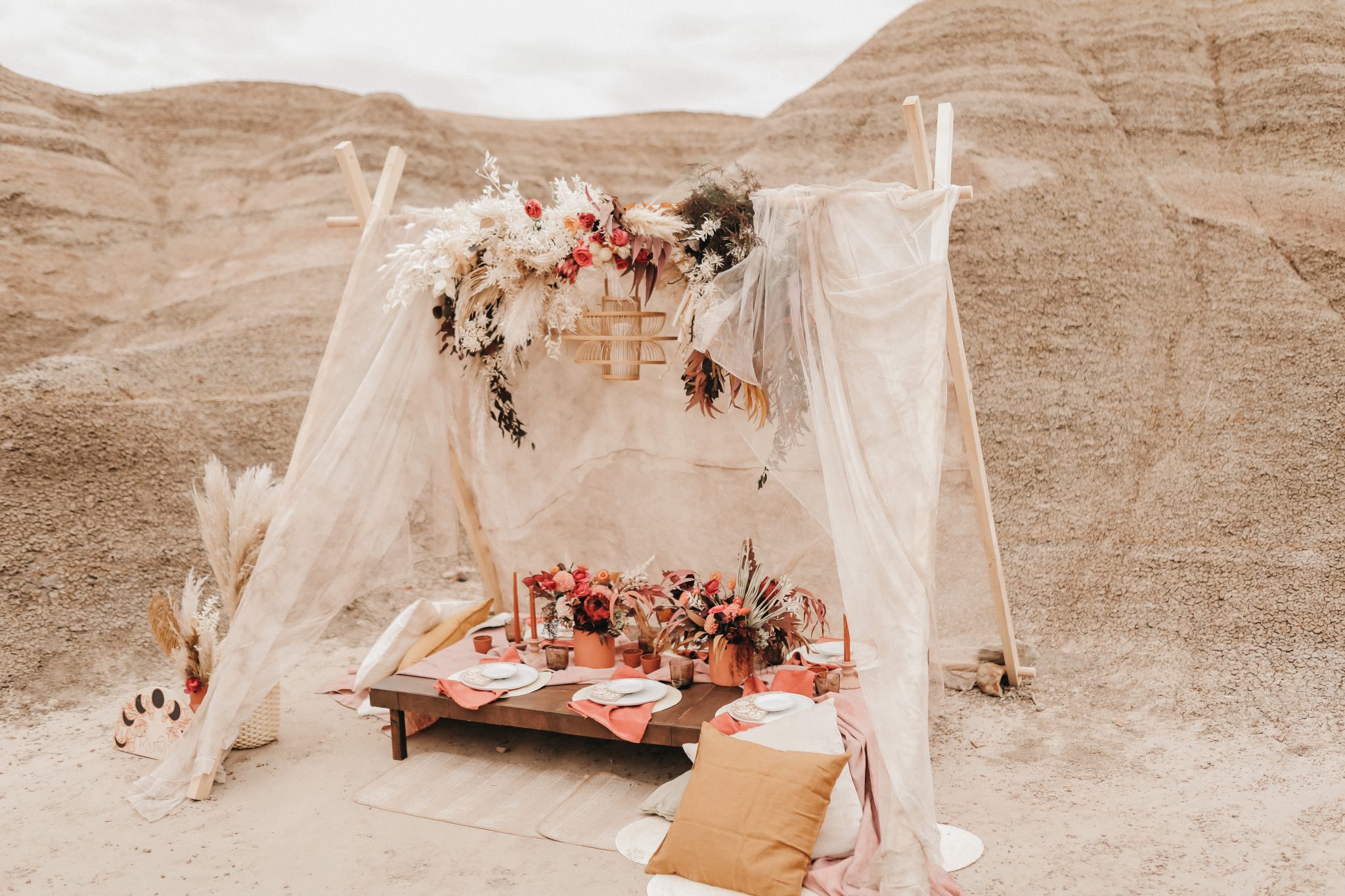 Boho styled tent with terracotta hues, a wicker chandelier and pillows for a Moroccan elopement inspiration