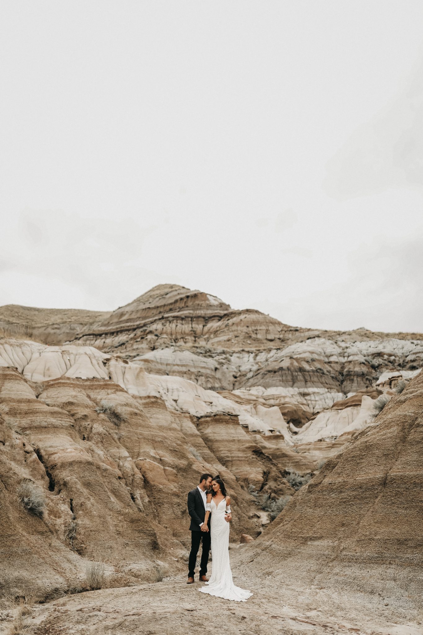 Bride and groom pose in front of the sand hills of Drumheller Alberta for Moroccan elopement inspiration