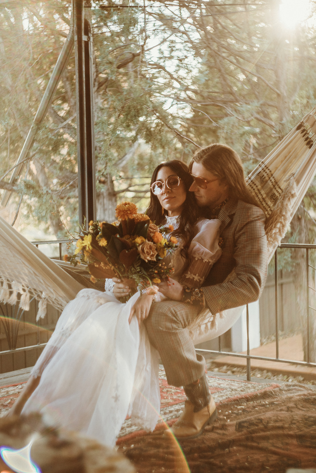 Dreamy retro inspired bride and groom in 70's attire share a moment on a macrame hammock