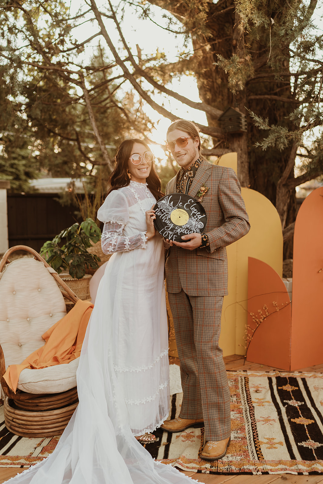 Retro inspired bride and groom pose in front of a groovy backdrop for their 70's Backyard Wedding Inspiration