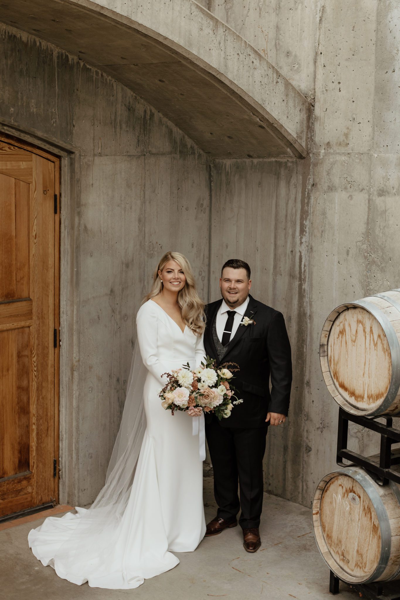 Classically styled bride and groom pose next to wine barrels on their wedding day