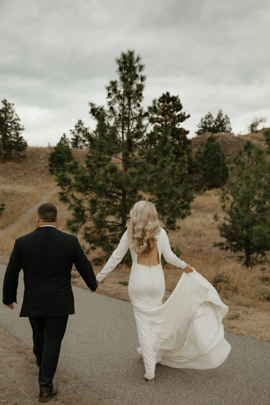 Bride and groom walk hand and hand through the hills of the Okanagan Valley