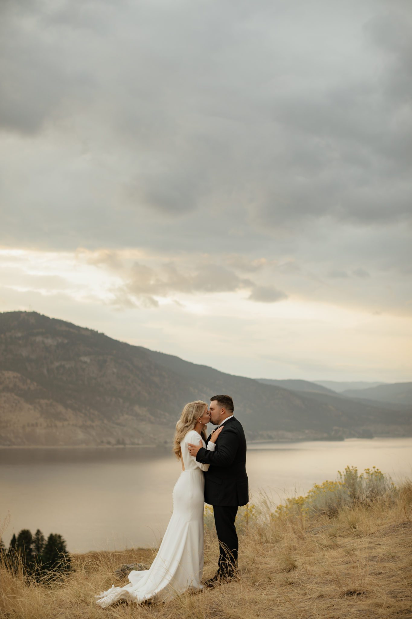 Bride and groom share a kiss at sunset with the Okanagan Valley behind them