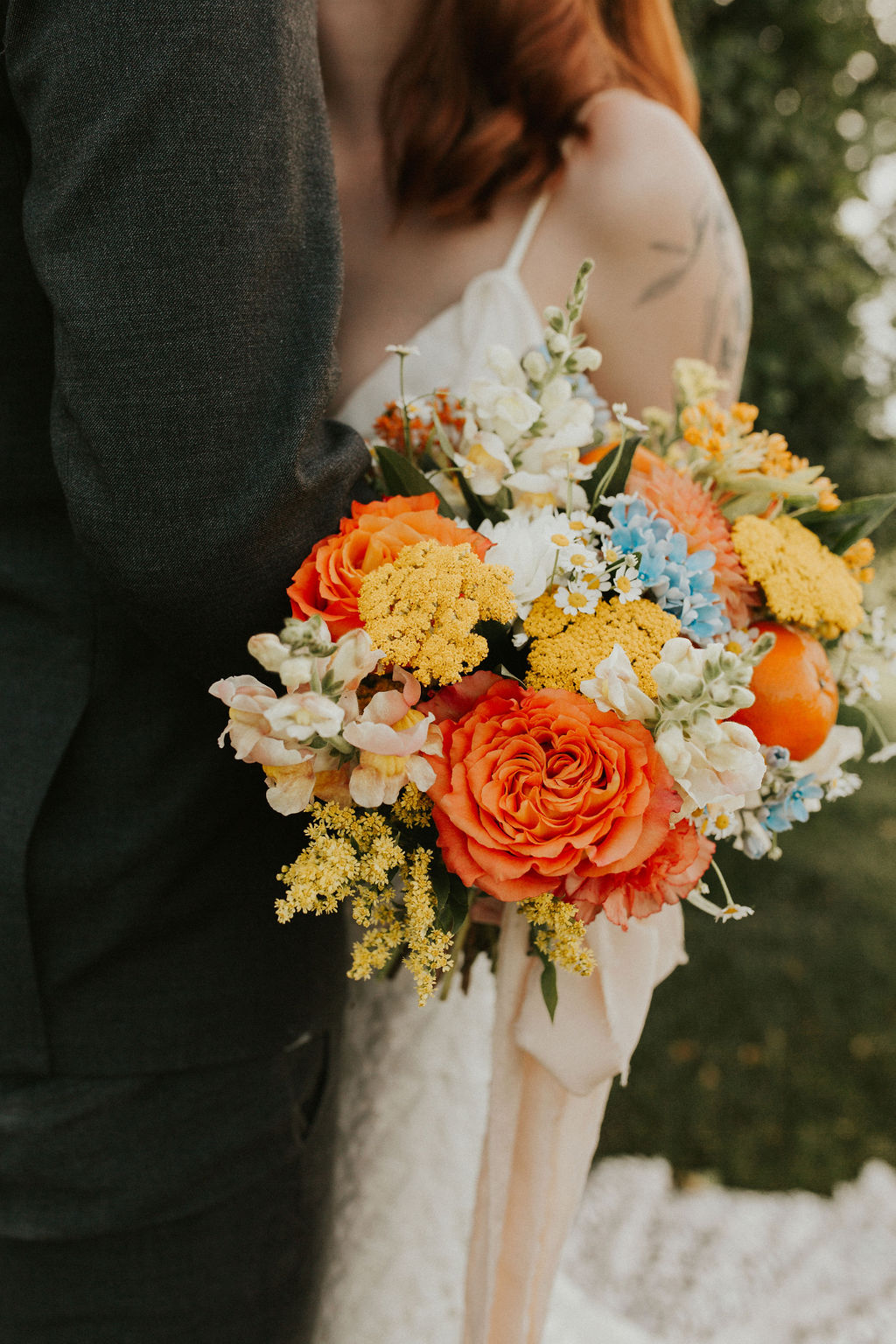 Bold summer wedding bouquet with tangerine, yellow, orange, and peach hues with a dash of blue