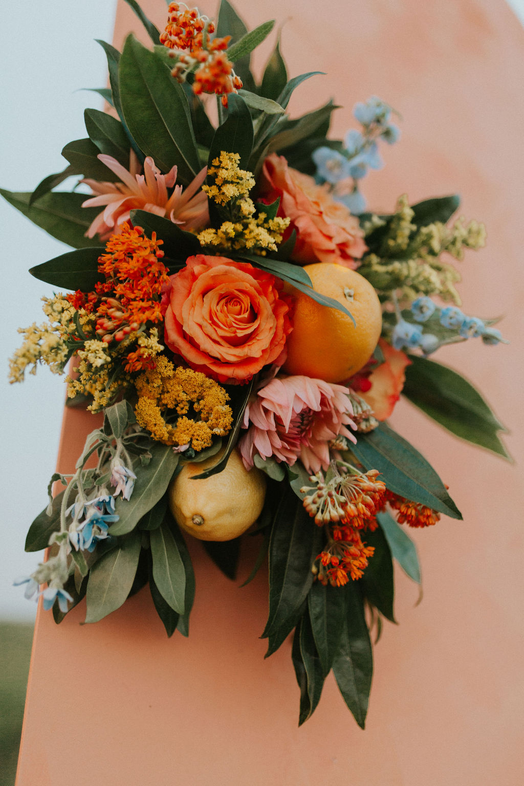 Tangerine inspired floral arrangement attached to a painted wooden panel backdrop
