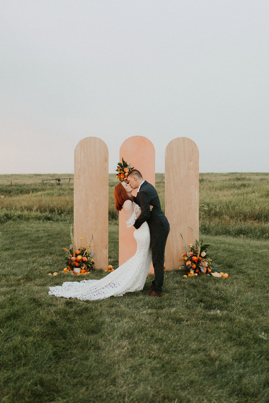 Bride and groom share a first kiss in front of their unique wooden panel backdrop for their tangerine inspired wedding