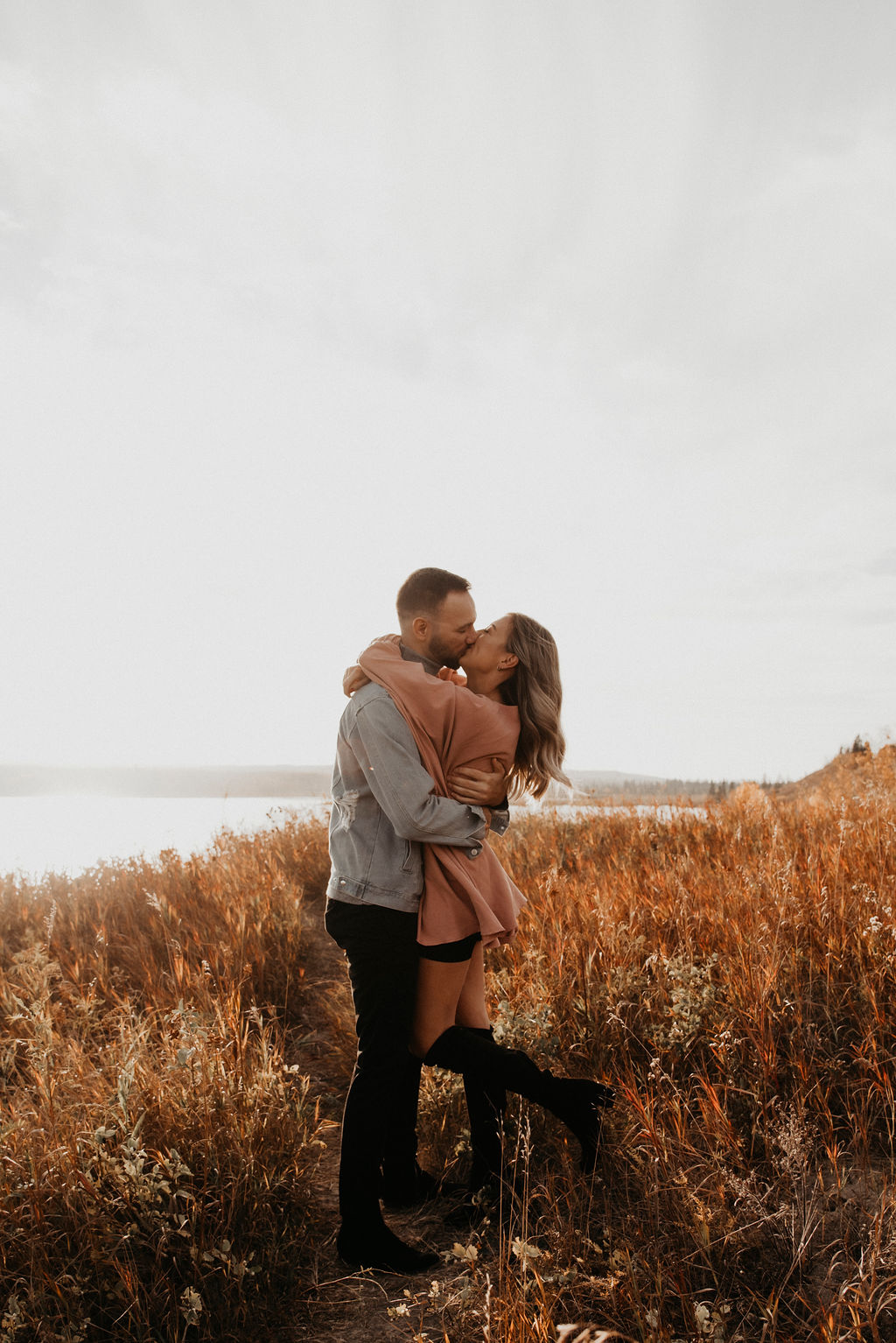 Sunset engagement session in a grassy field with engagement session outfit inspiration with a blush dress and denim shirt
