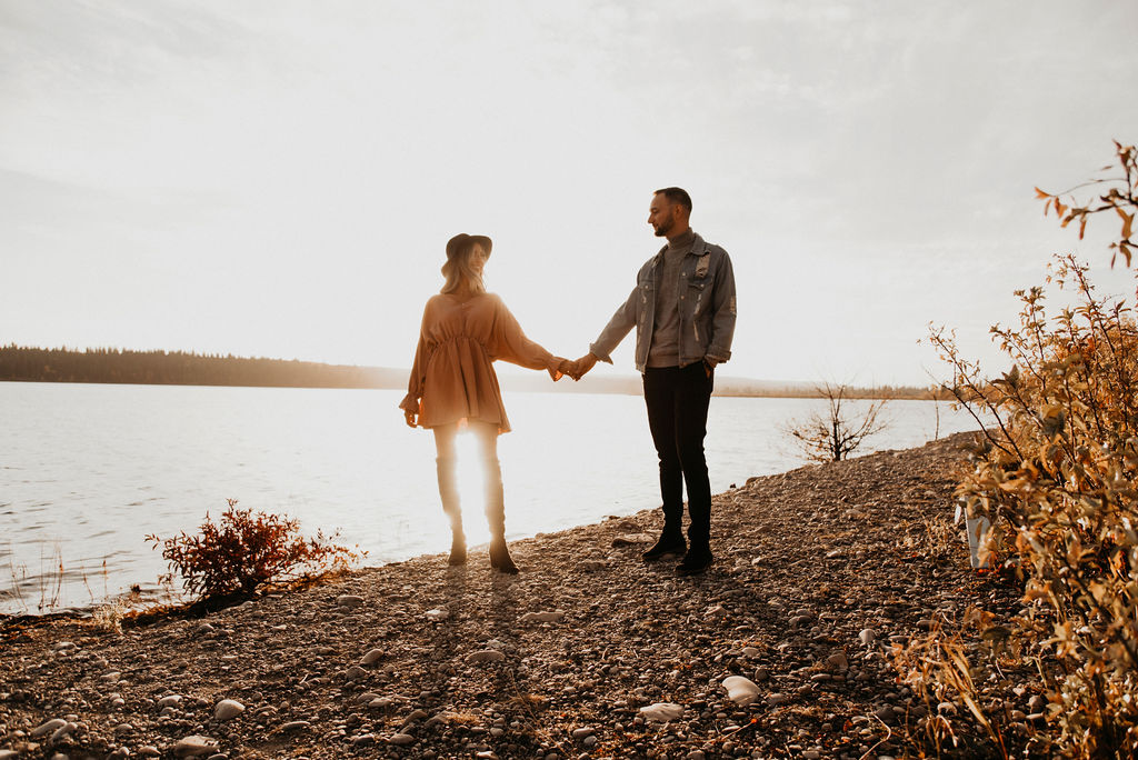 Newly engaged couple hold hands next to a lake for their sunset engagement session