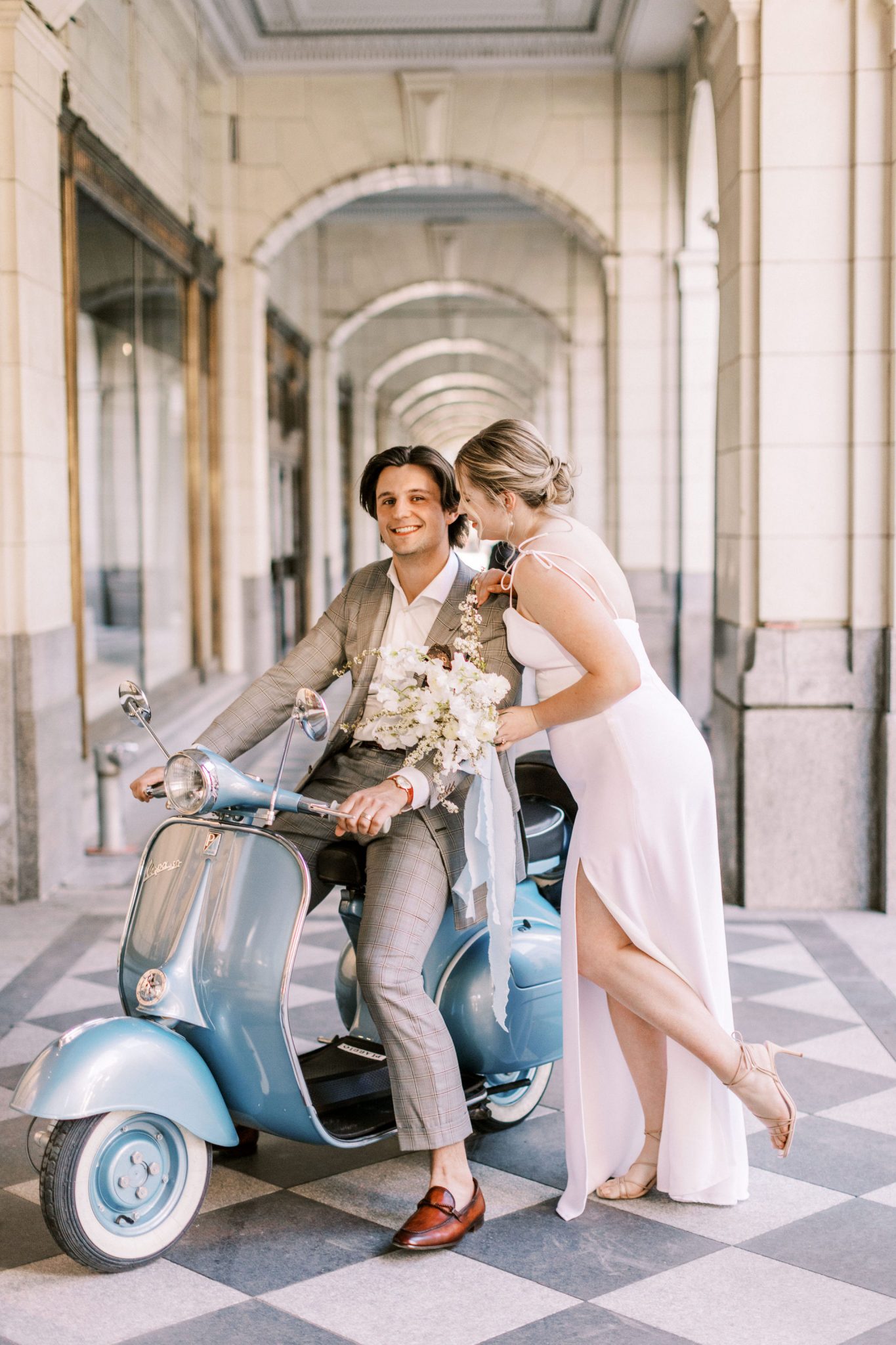 Modern bride in a white slip dress and groom in a grey suit pose with a blue vespa for this downtown elopement