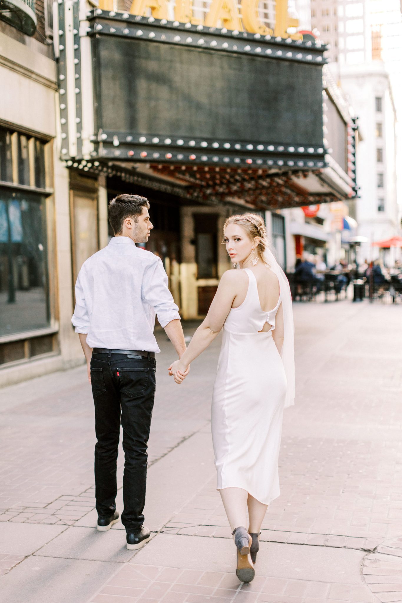 Modern bride in a cut out back dress walk hand in hand on the streets of downtown Calgary for this modern elopement