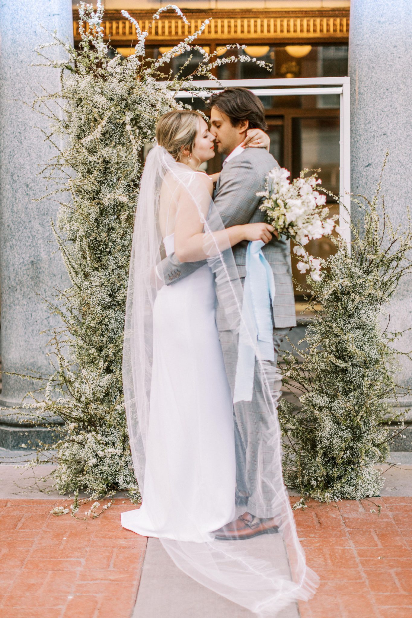 Bride and groom share a kiss in downtown Calgary in front of a greenery inspired floral installation with robin blue accents