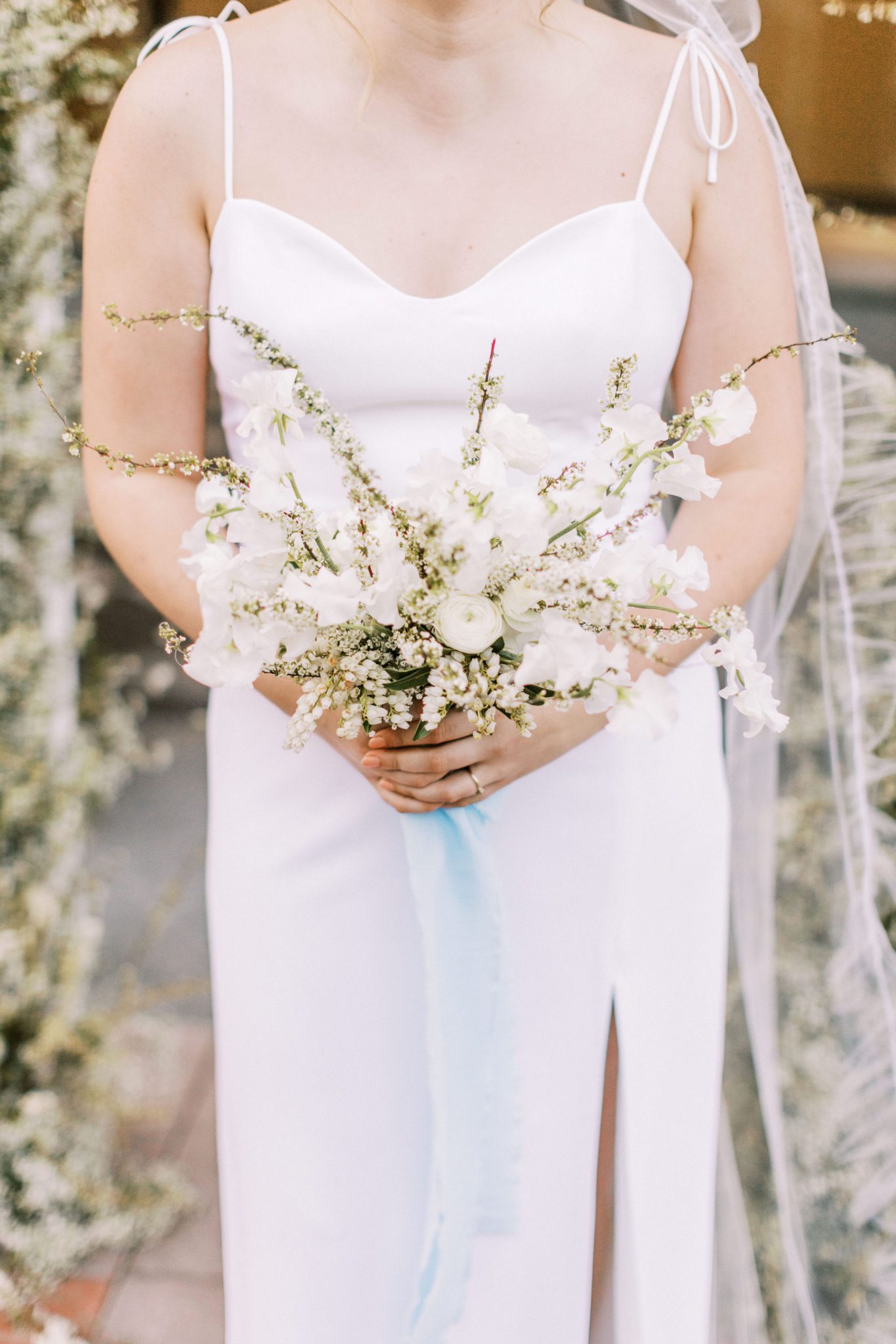 Modern bride in a white slip dress holding a monochromatic white bouquet with a blue ribbon