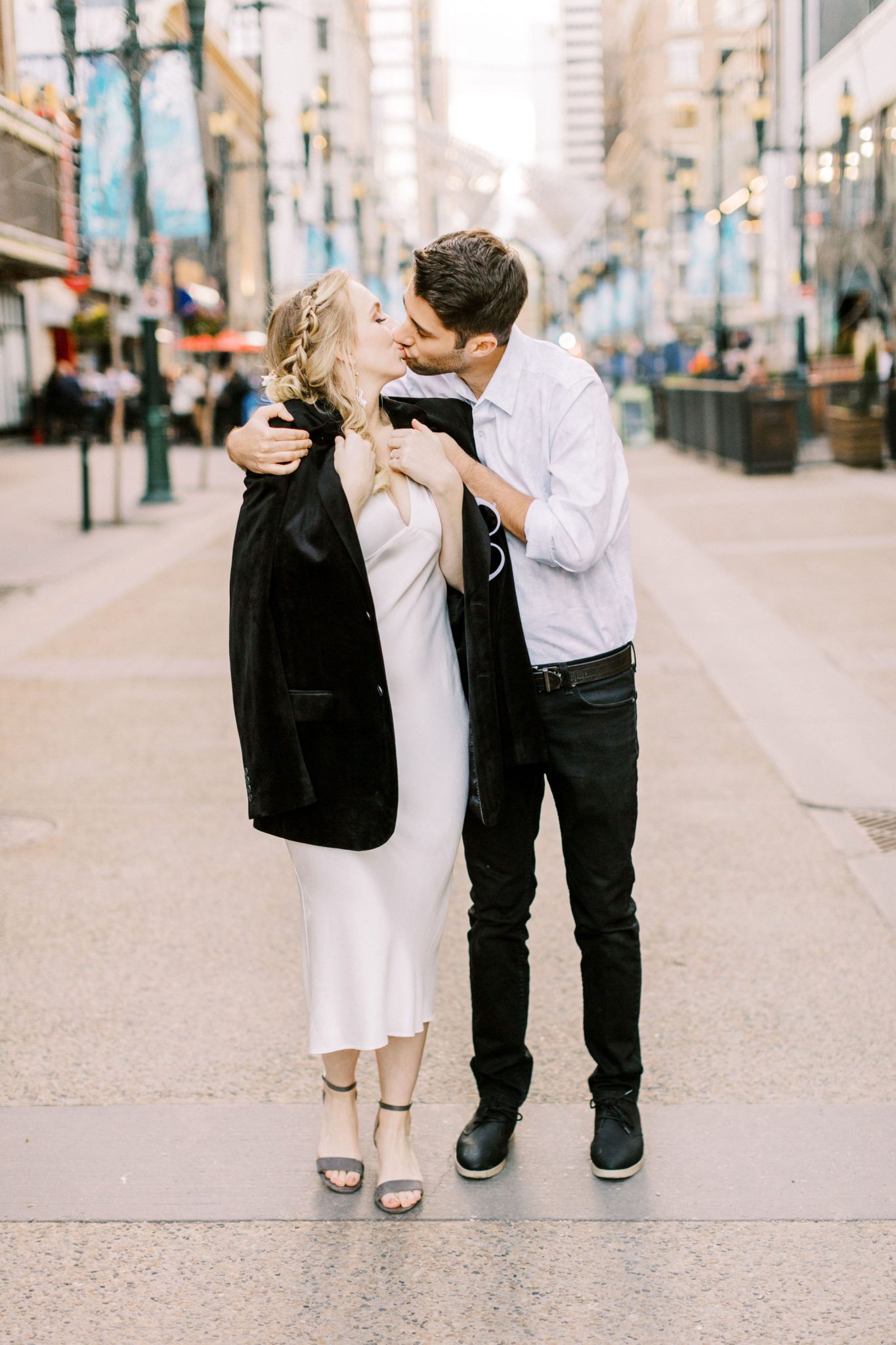 Modern bride and groom with a black velvet jacket share a kiss on the streets of Calgary Alberta for this downtown elopement inspiration