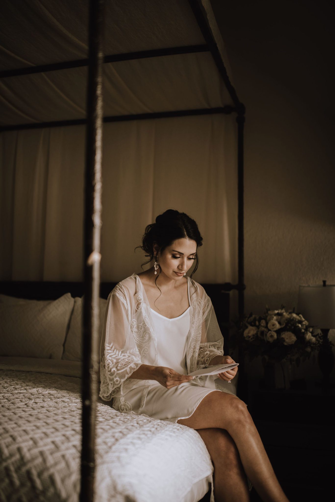 Bride sits on a four poster bed reading a letter from her groom on the morning of her wedding day