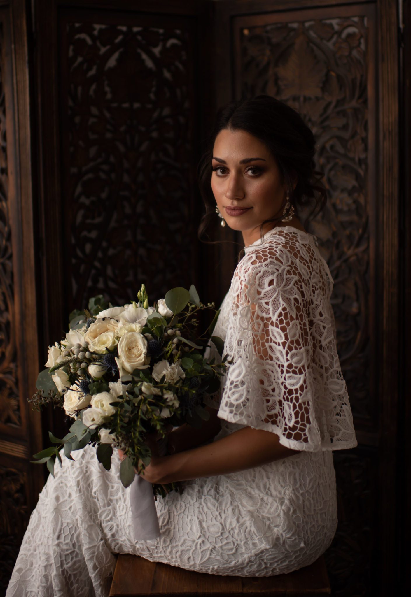 Vintage inspired bride poses in front of an ornate hand carved wooden panel