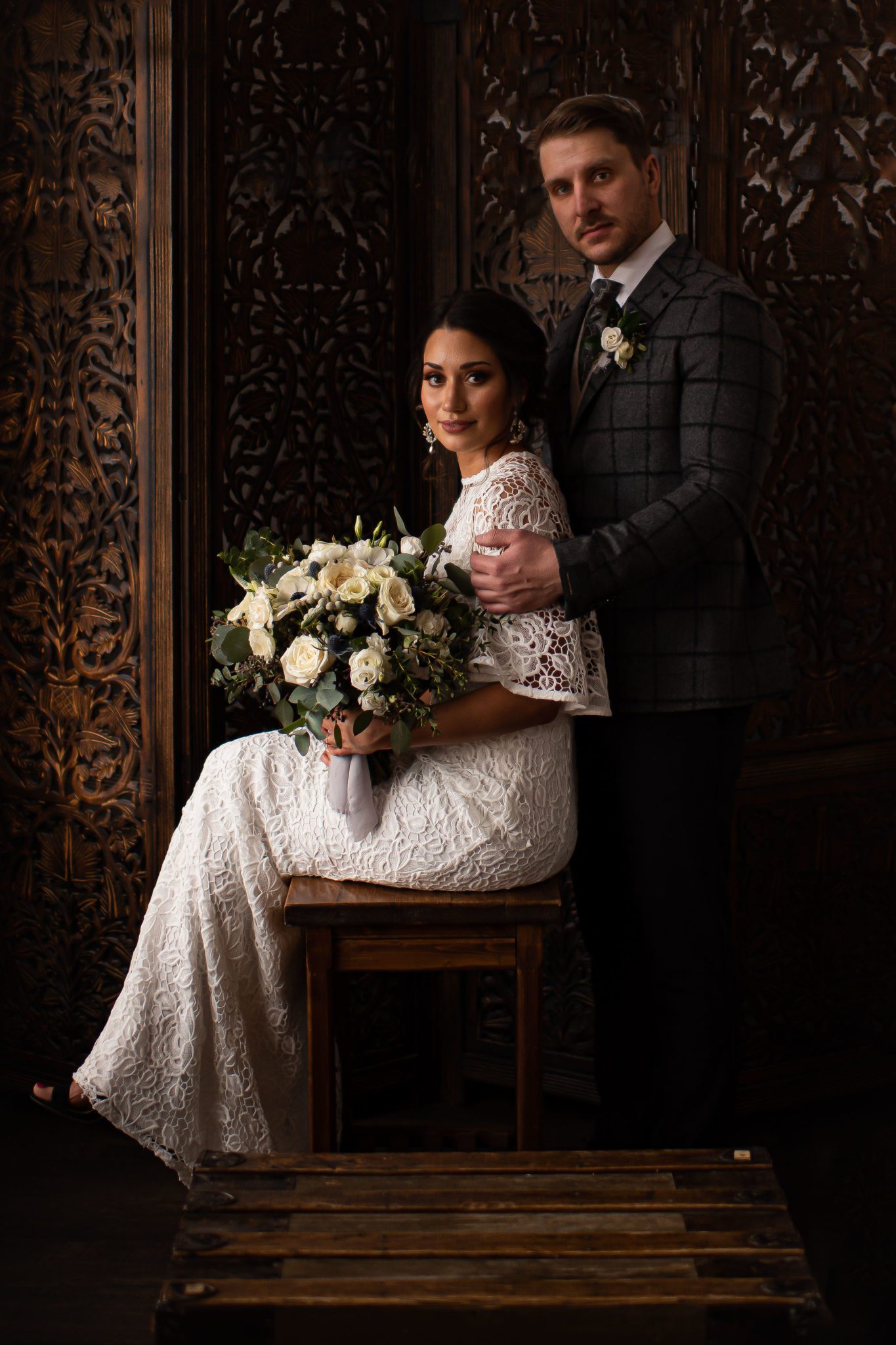 Baroque inspired wedding portrait of a bride and groom in front of an ornate hand carved wooden panel at A Bear & Bison Canadian Country Inn in Canmore Alberta 