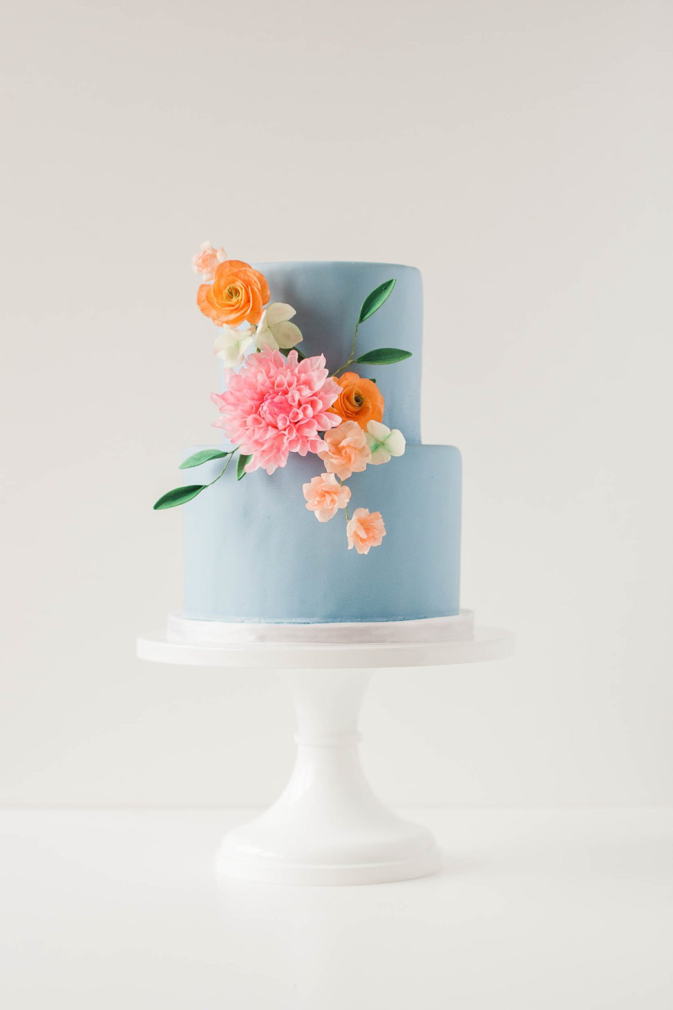 show-stopping wedding cake dusty blue two tiered cake with bright peach and tangerine sugar flower adornments