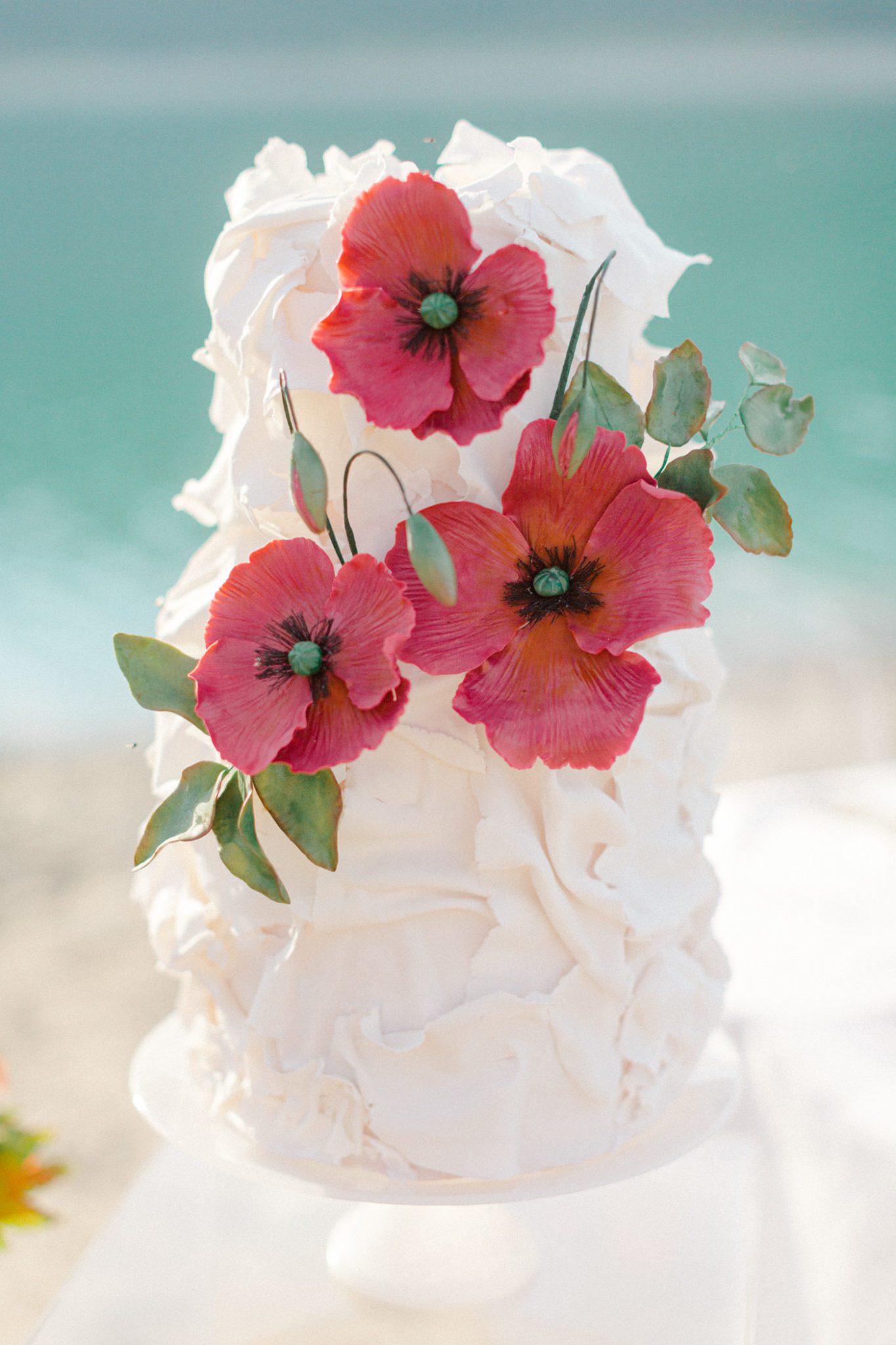 Bright red handmade sugar flower poppies on a white ruffled wedding cake