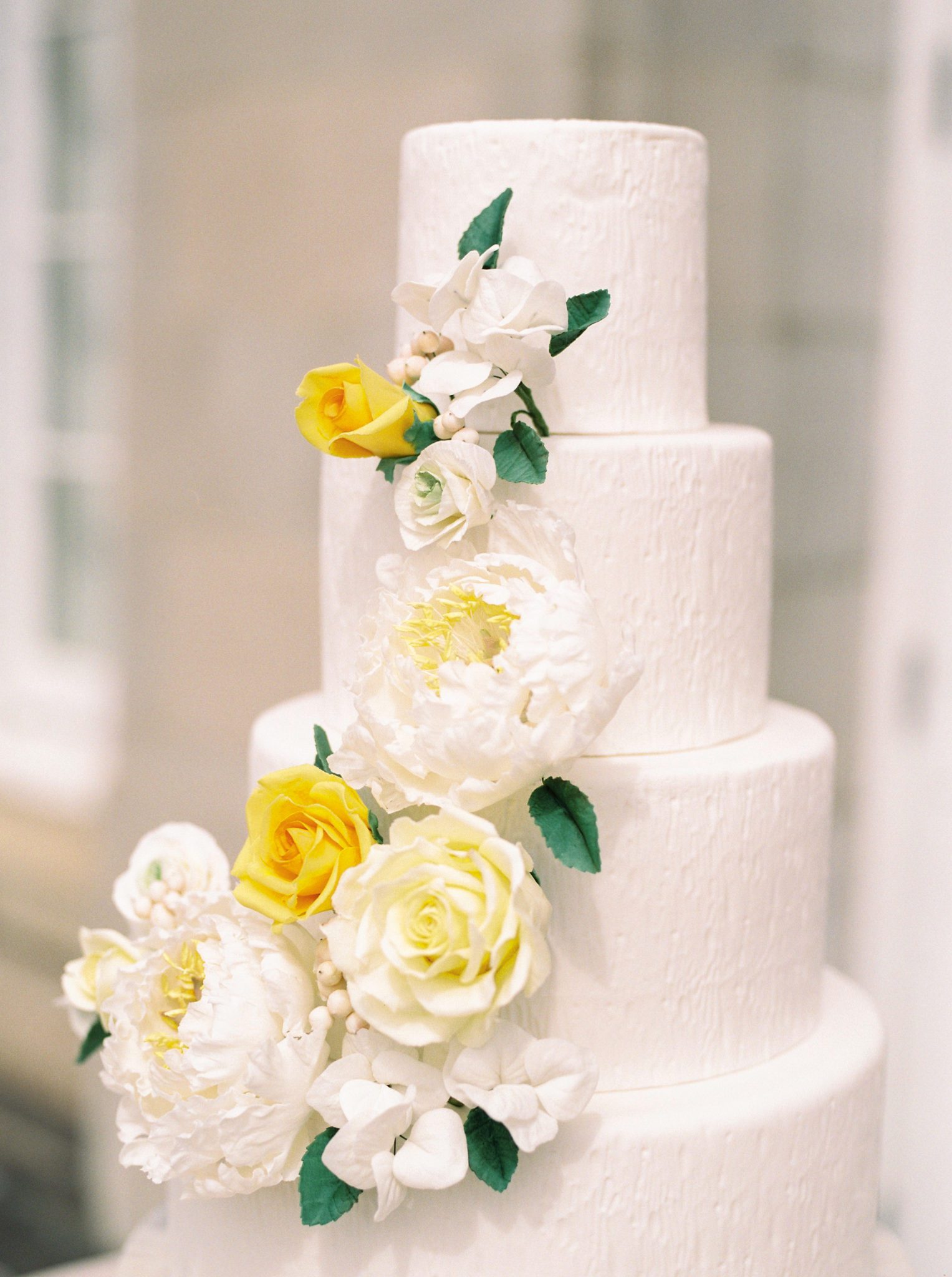 Yellow and white sugar flowers on a three tiered white wedding cake