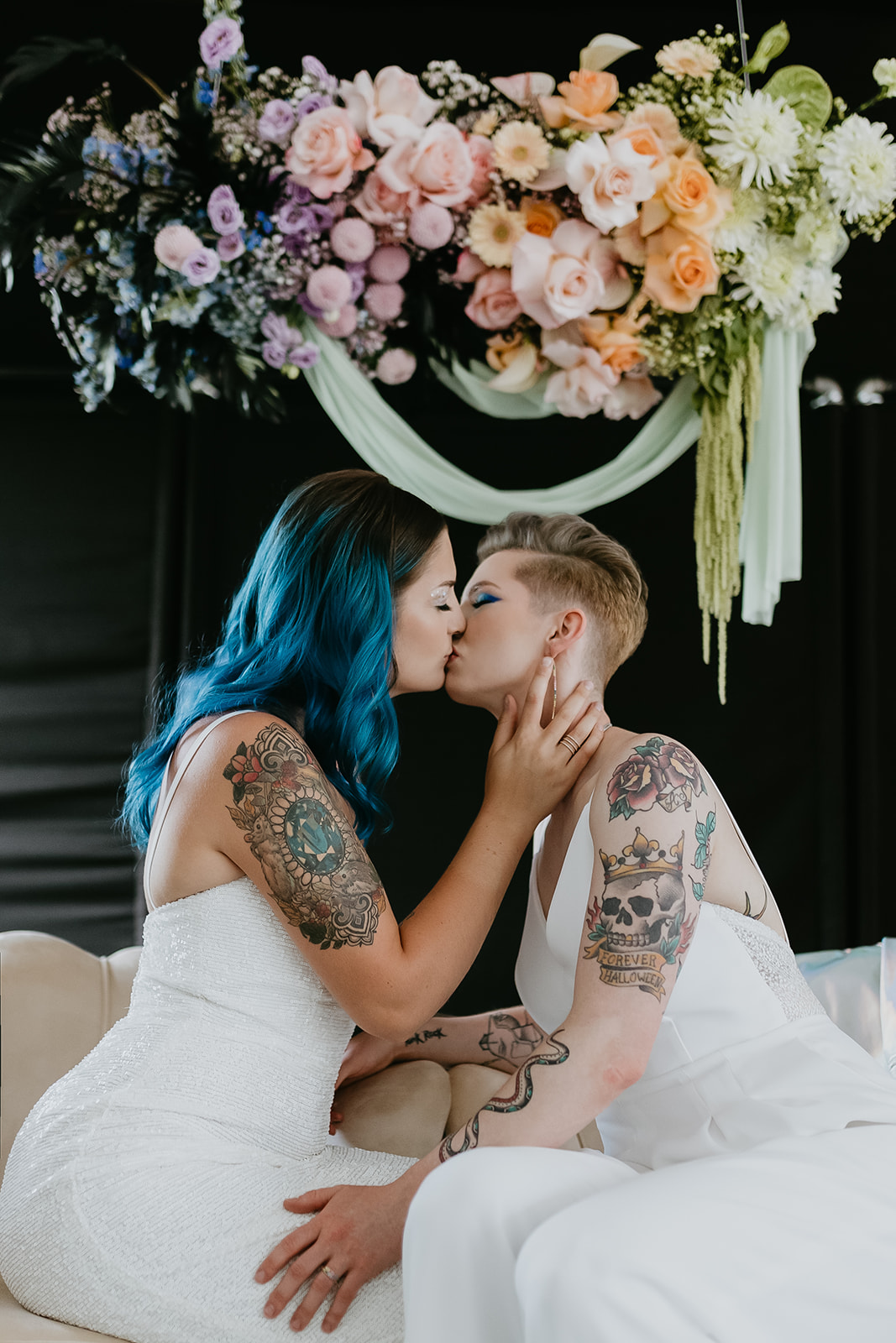 Rocker styled tattooed brides kiss in front of a bold Holographic inspired floral installation