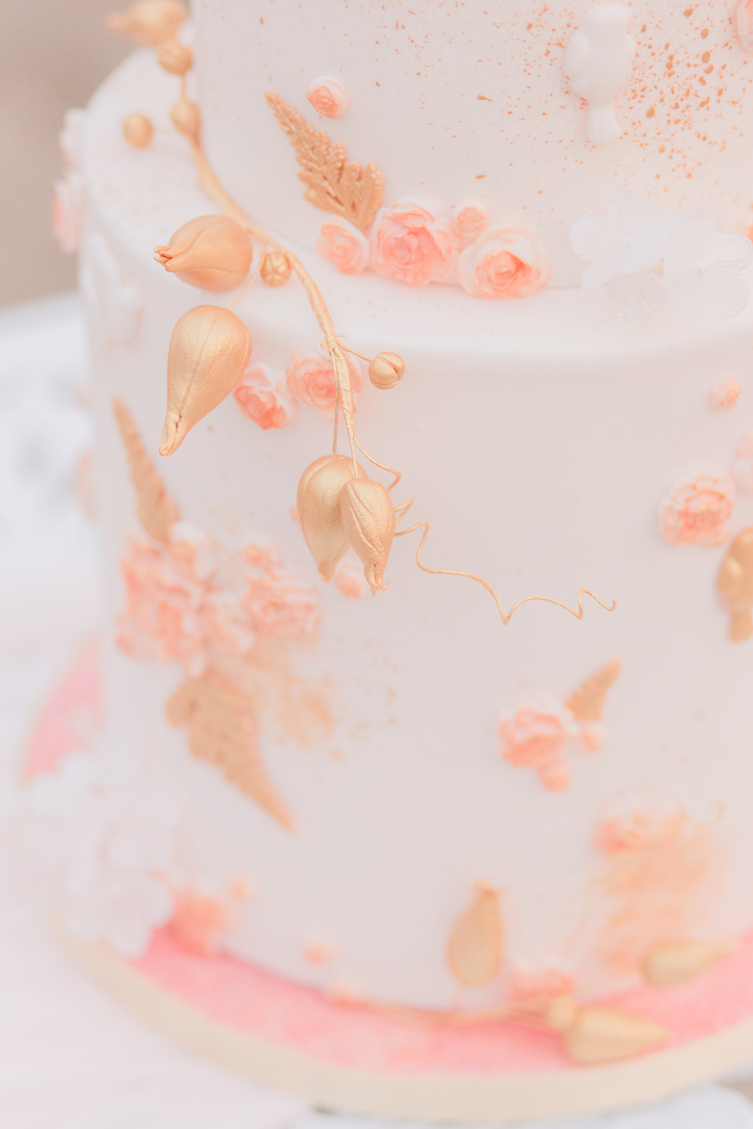 Pink and gold floral details on a two tiered white wedding cake